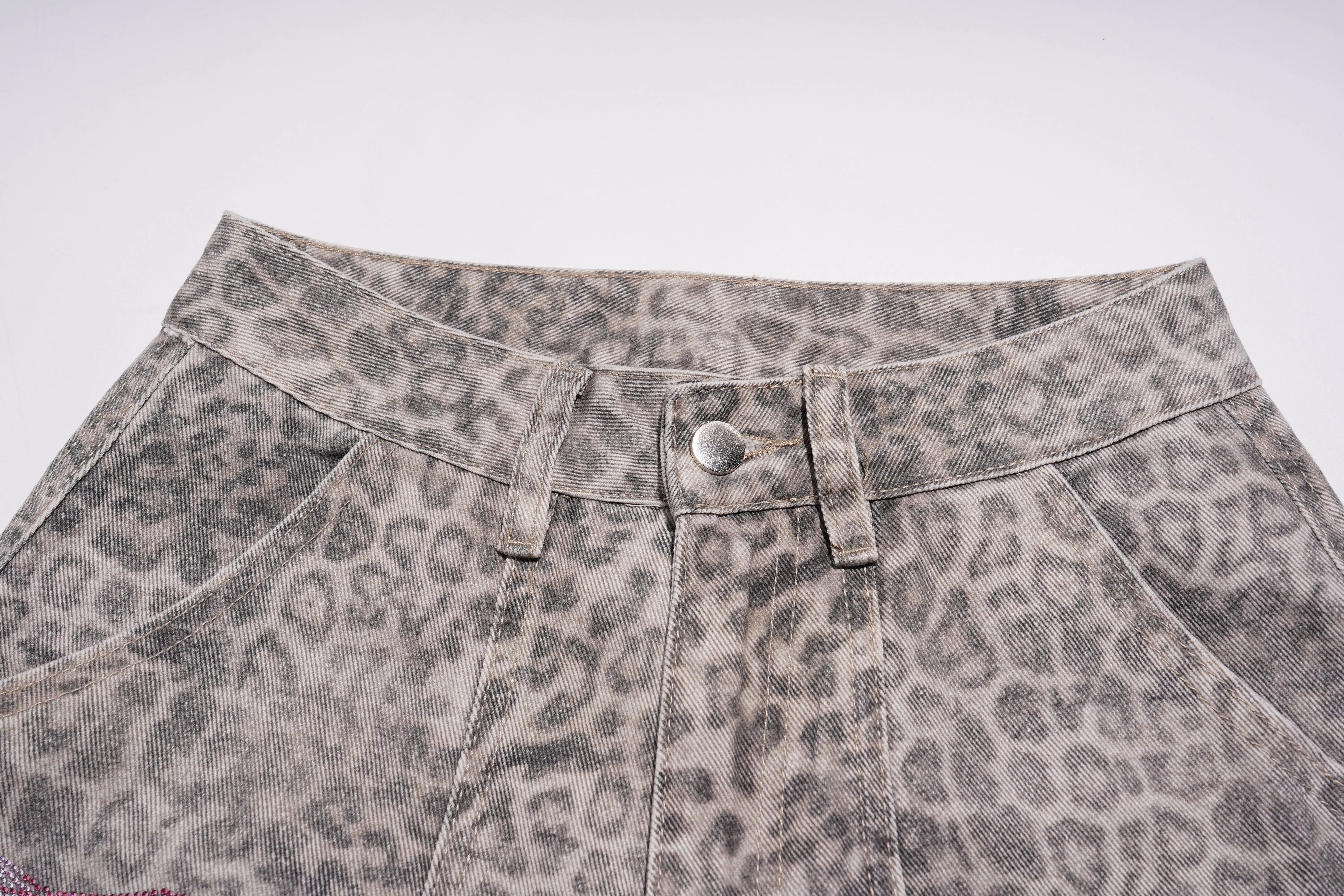 Leopard print denim fabric with button and stitching details on a white background, TCH Grey Leopard Rhinestone Wings Wide-Leg Jeans
