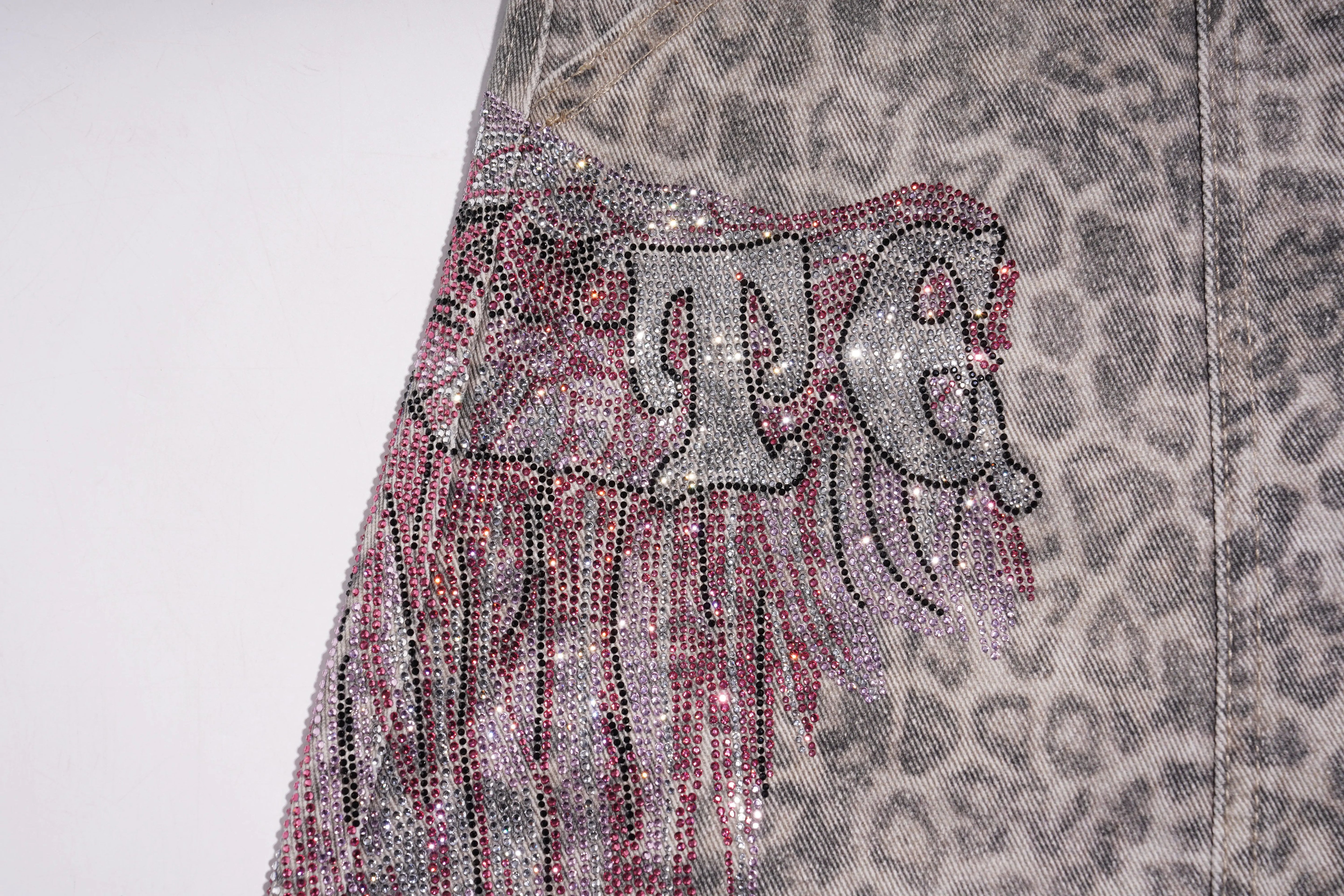 Close-up of a fabric with rhinestone lettering and leopard print pattern. TCH Grey Leopard Rhinestone Wings Wide-Leg Jeans