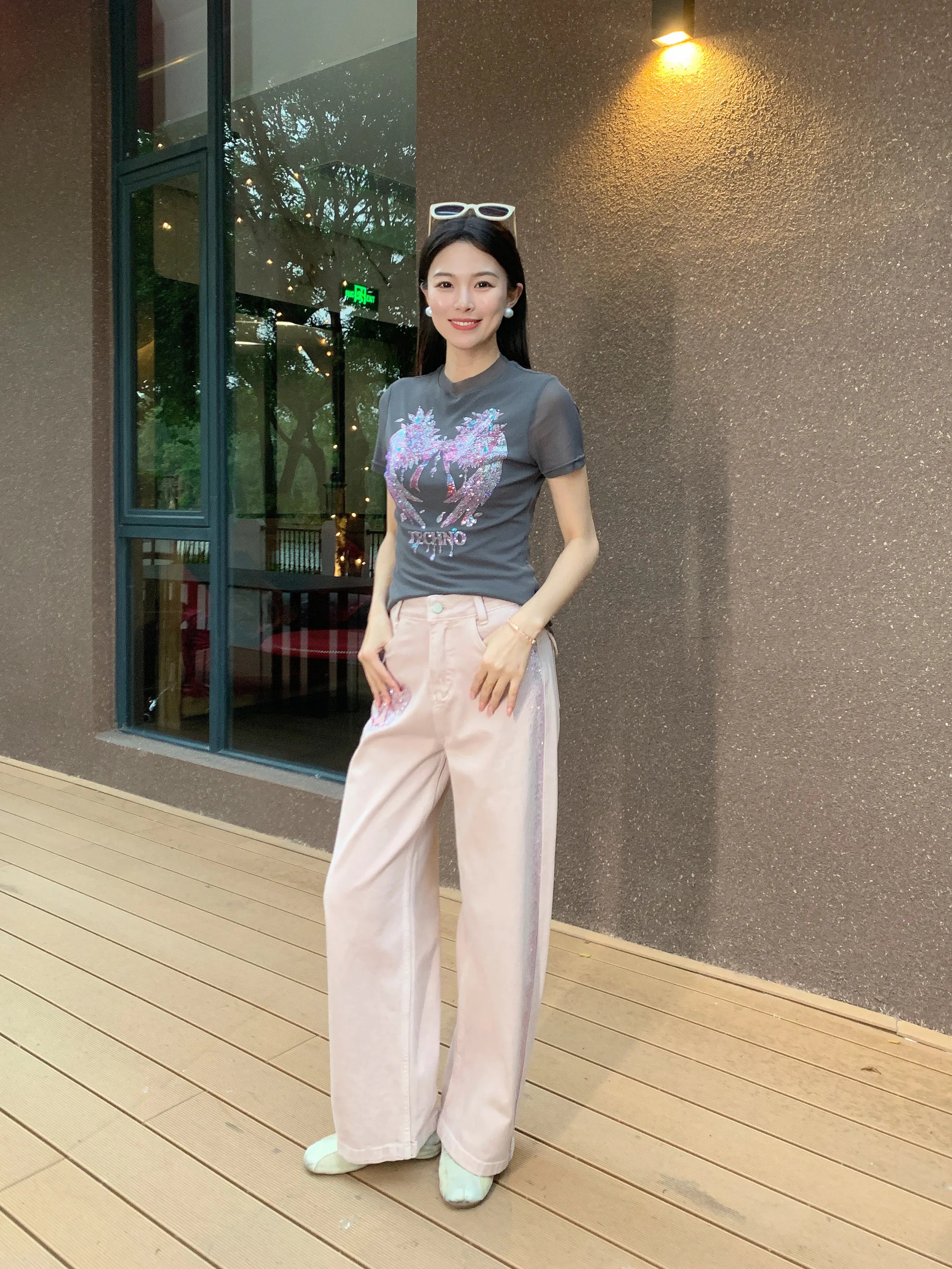 Woman standing on a wooden deck wearing a gray t-shirt and light pink pants. TCH Grey Rhinestone Pink Wings Graphic T-Shirt