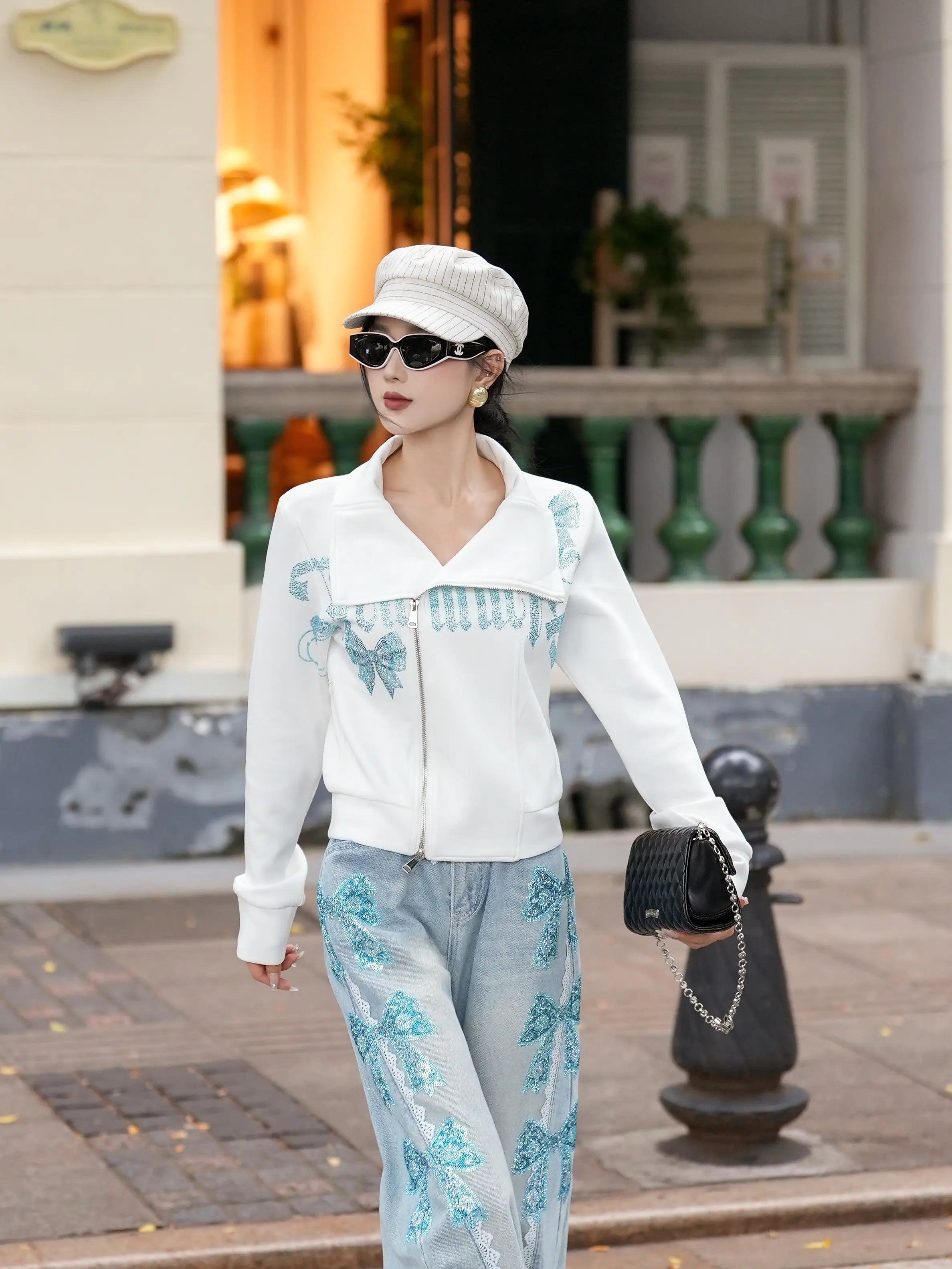 Woman in white outfit with blue patterns walking outdoors. TCH Ice Blue Rhinestone Bow Zip-Up Jacket