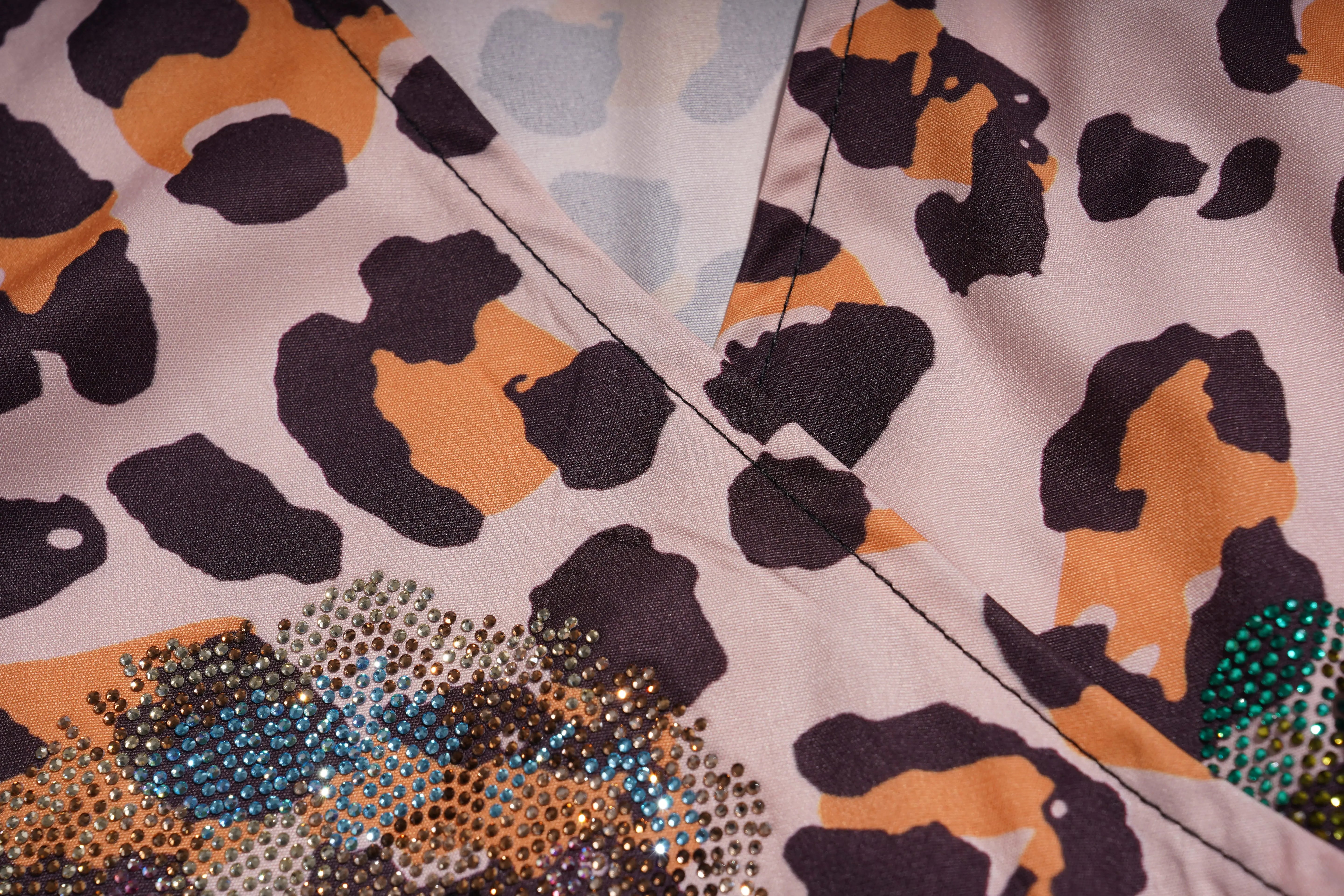 Close-up of fabric with a pattern of black, orange, and blue shapes on a light background. TCH Leopard Rhinestone Animal Embellished Dress