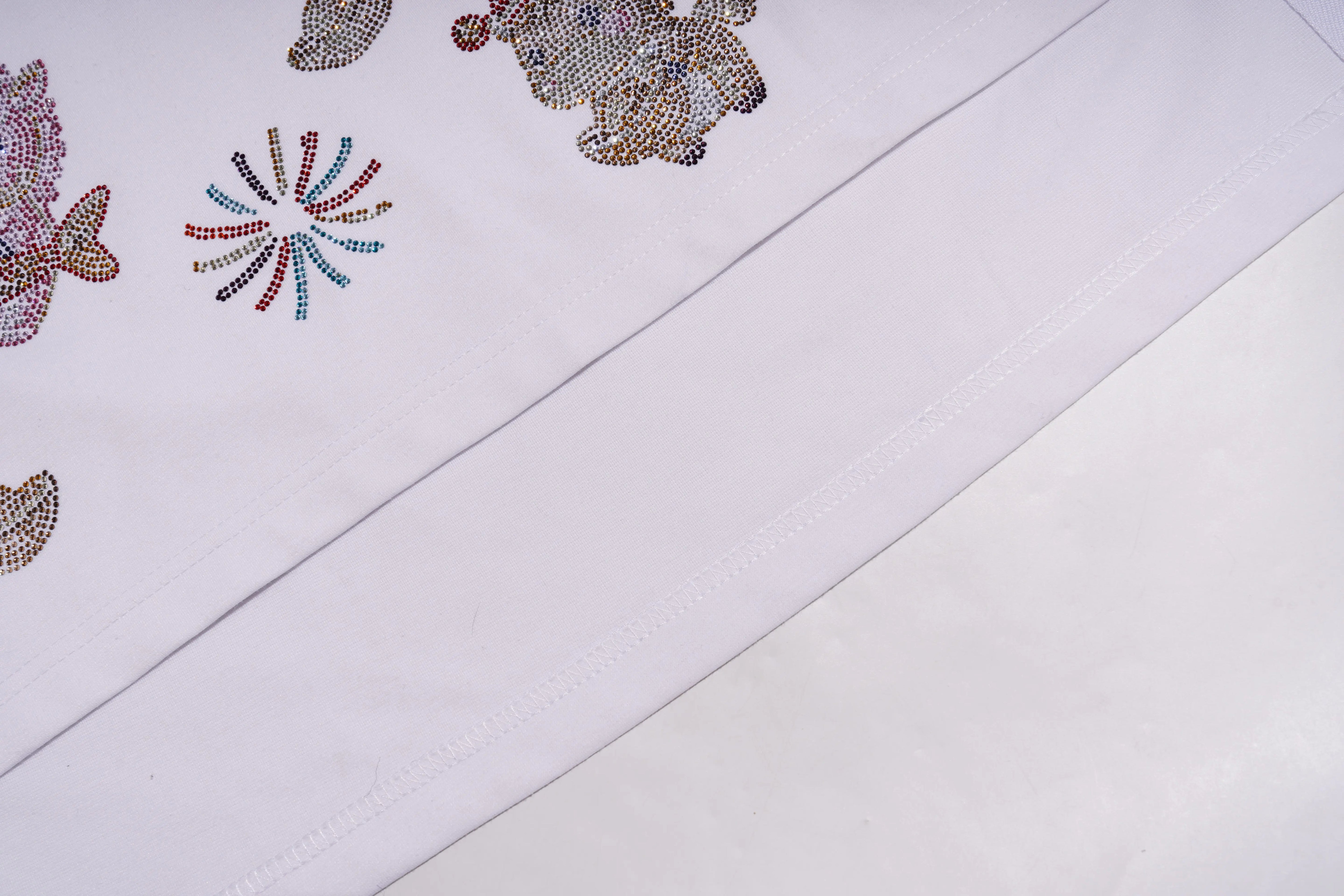 Close-up of a white fabric with decorative floral patterns made of colorful beads. TCH Lucky Pony Rhinestone Sleeveless Polo Shirt