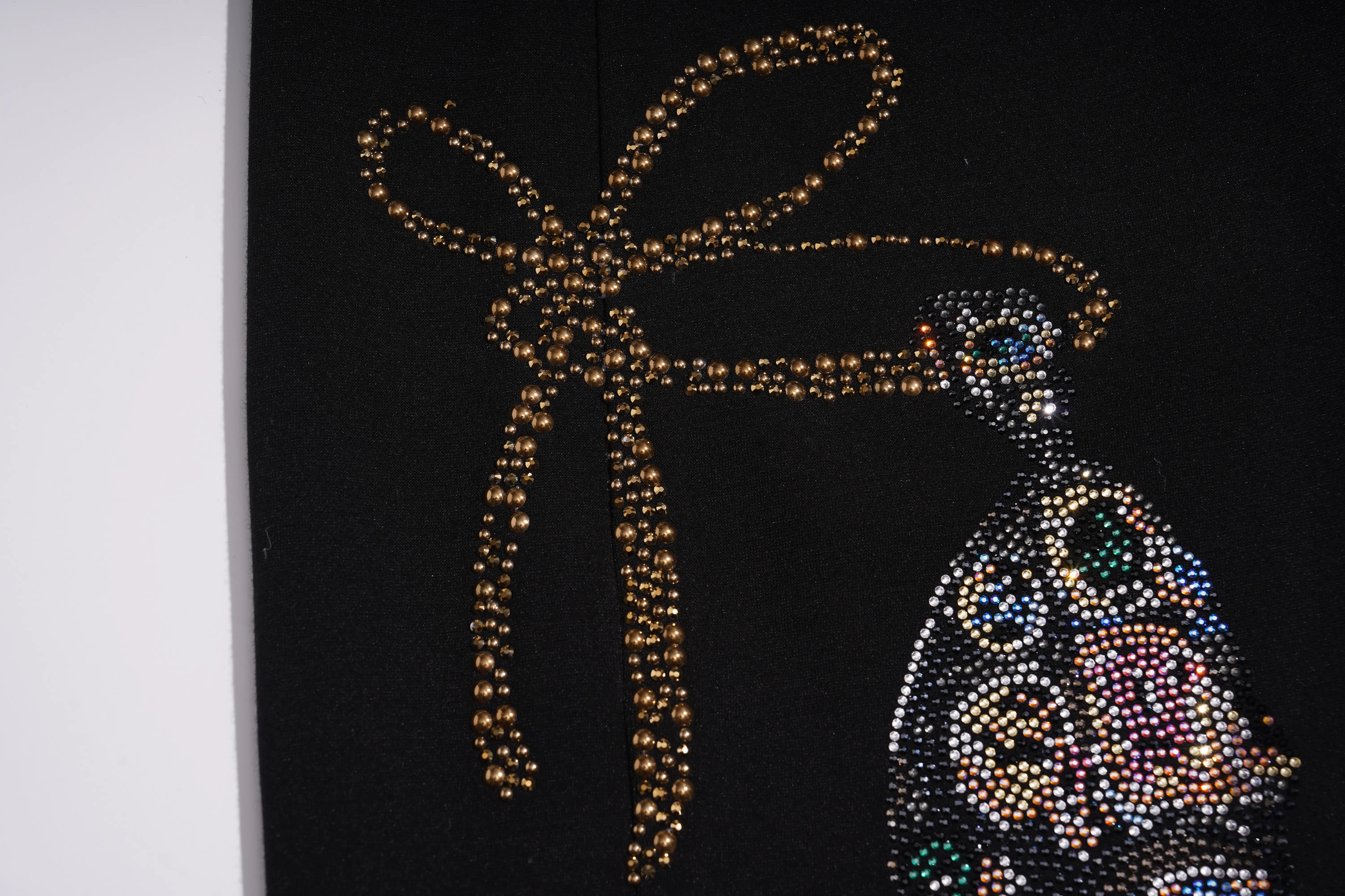 A close-up of a black garment featuring a large bow and bird embellishments made of gold-toned beads and iridescent rhinestones. TCH Luxury Rhinestone High Heel Graphic Black Sweatpants