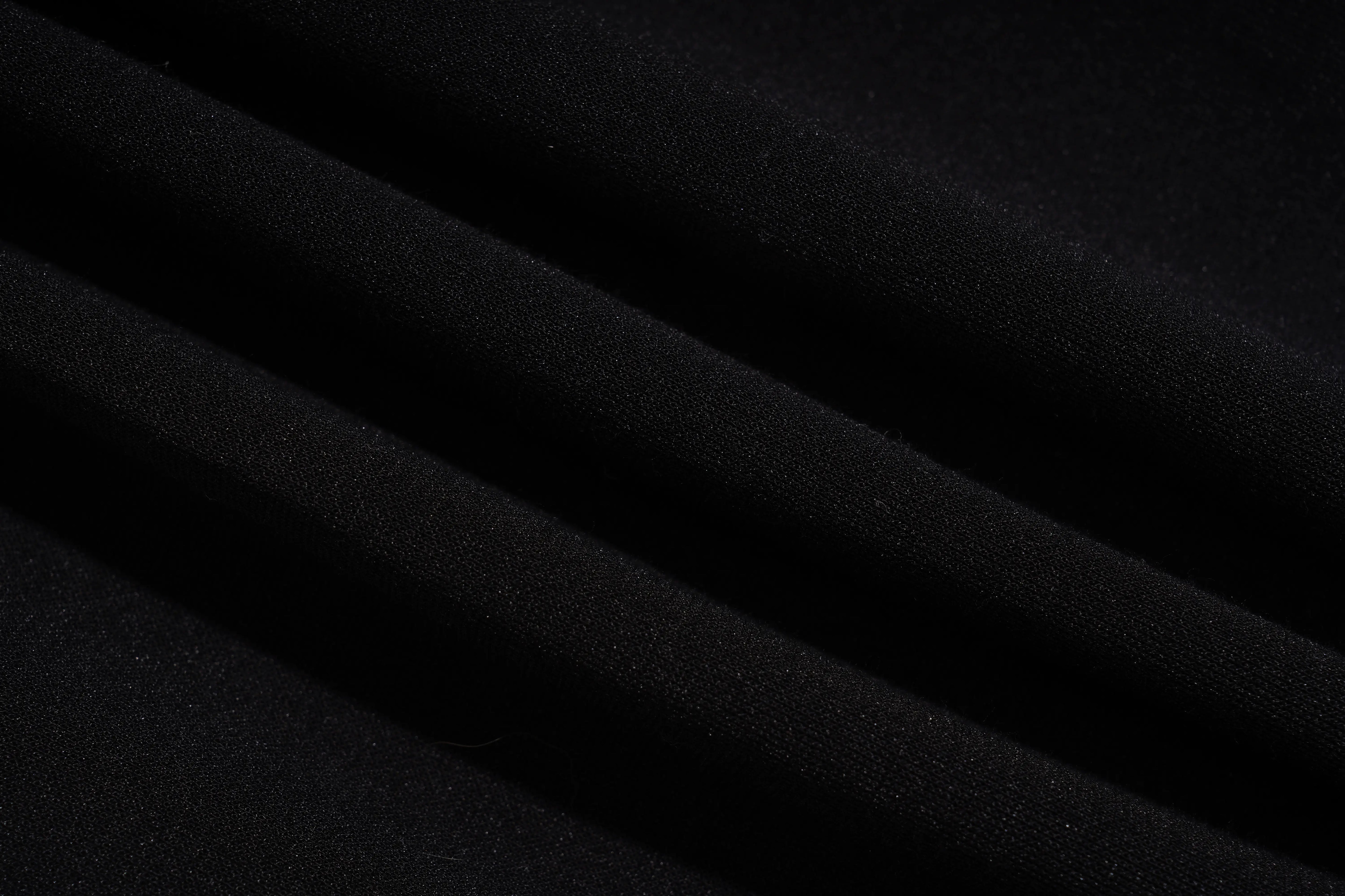 A close-up of draped black fabric with soft diagonal folds and a smooth matte texture. TCH Luxury Rhinestone High Heel Graphic Black Sweatpants