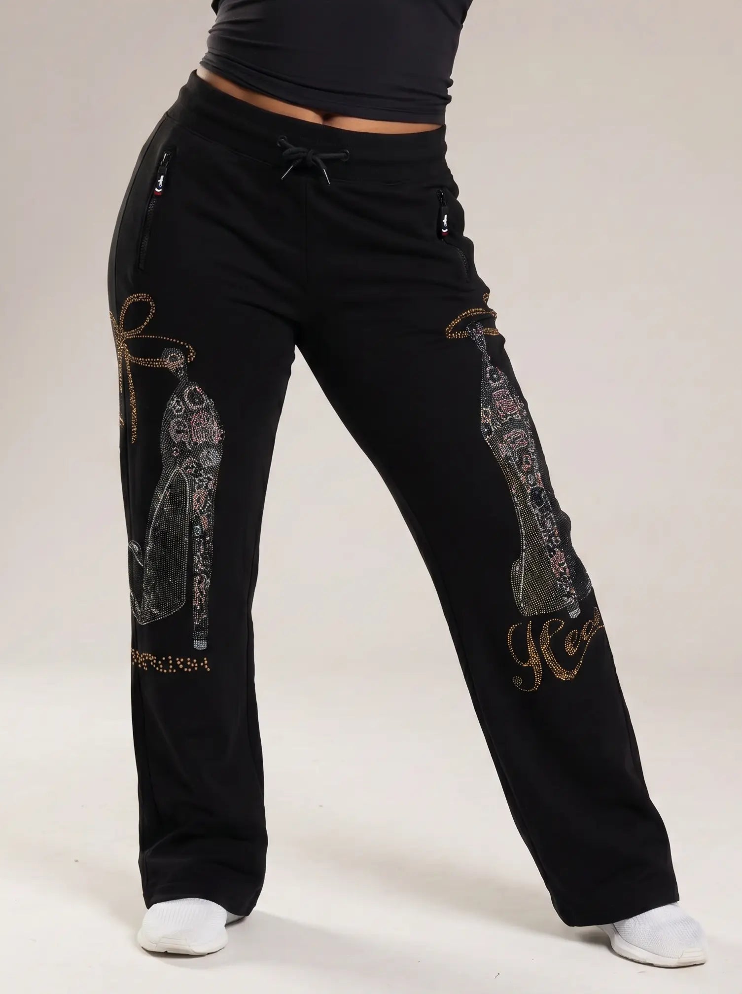 Black wide-leg sweatpants with decorative paisley and script embellishments on the legs, shown on a model from the waist down against a light beige studio background. TCH Luxury Rhinestone High Heel Graphic Black Sweatpants