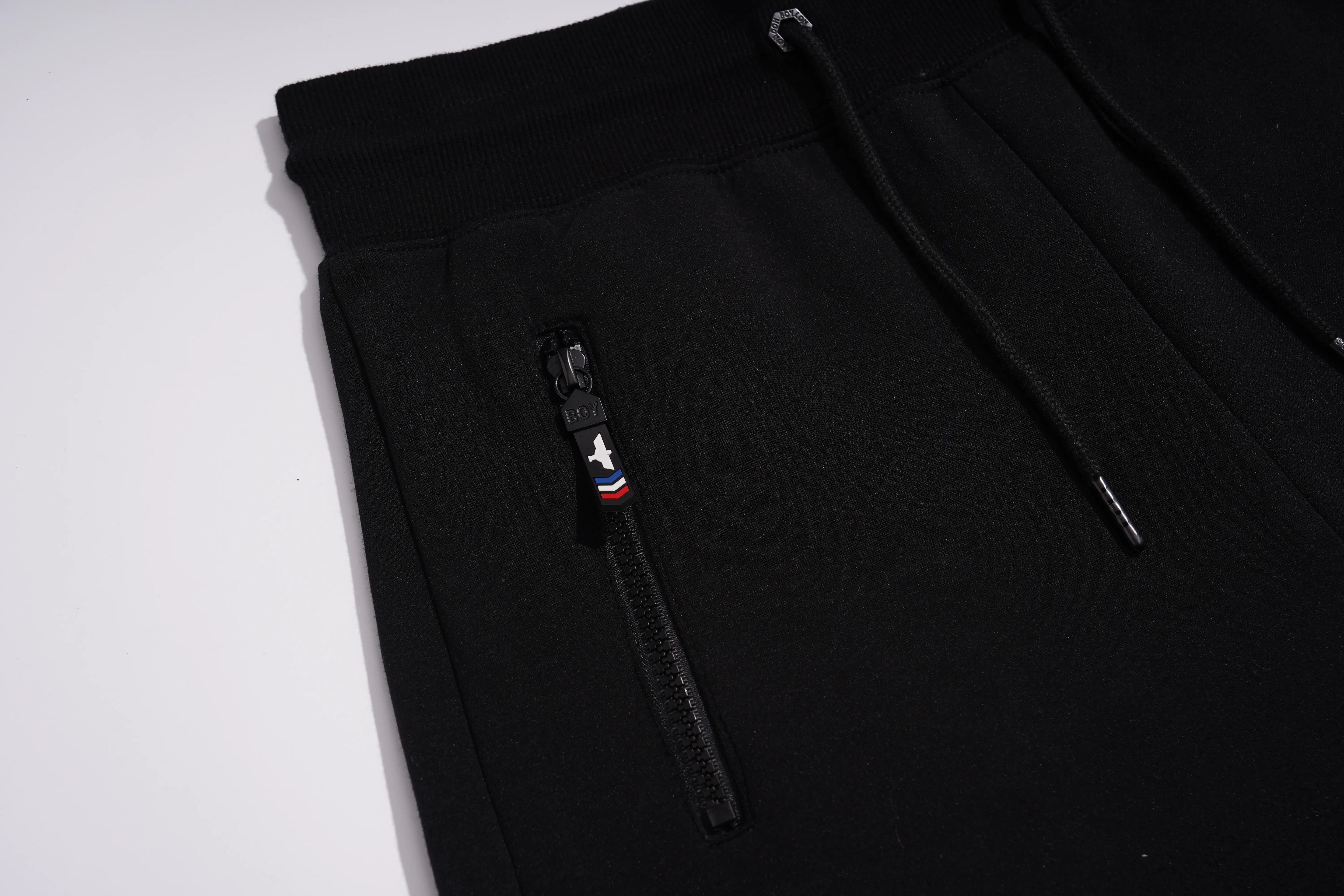 Close-up of black drawstring sweatpants showing a zippered pocket with a black zipper pull and white drawstring cords on a white background. TCH Luxury Rhinestone High Heel Graphic Black Sweatpants