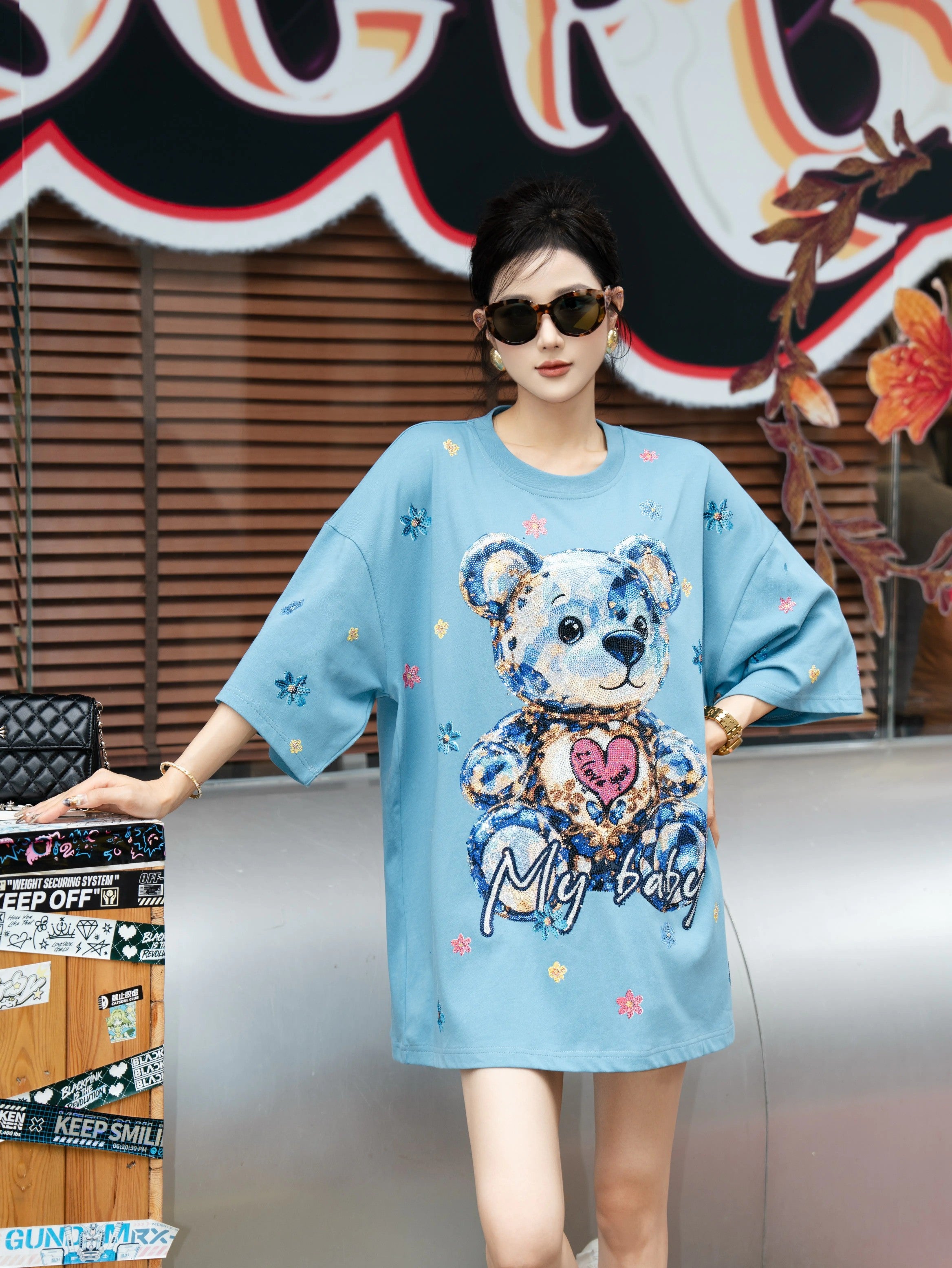 Woman wearing a blue dress with a teddy bear design in an urban setting. TCH My Baby Rhinestone Bear Oversized Blue T-Shirt