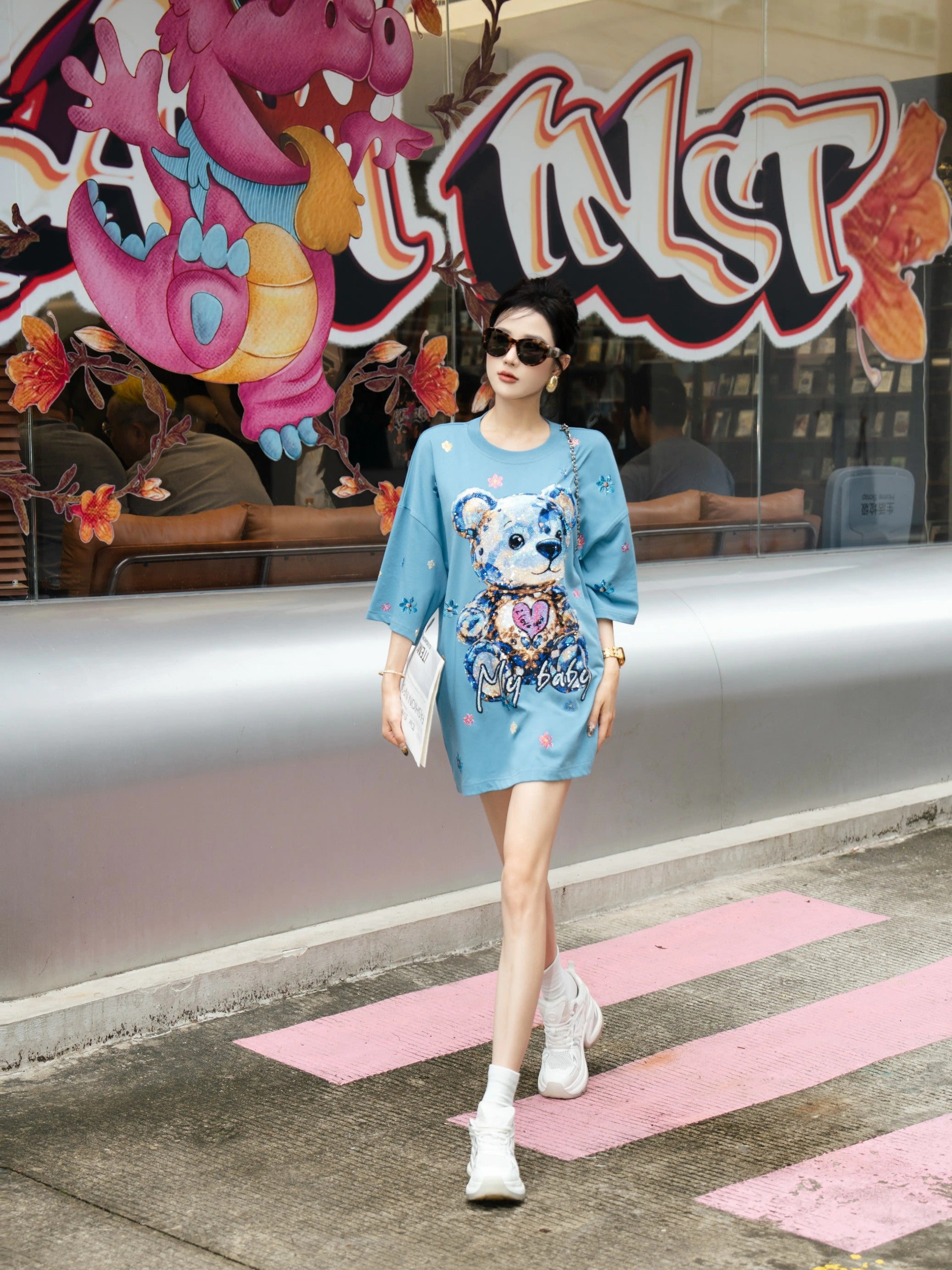 Woman in a blue dress with a colorful design walking on a street with a vibrant background. TCH My Baby Rhinestone Bear Oversized Blue T-Shirt