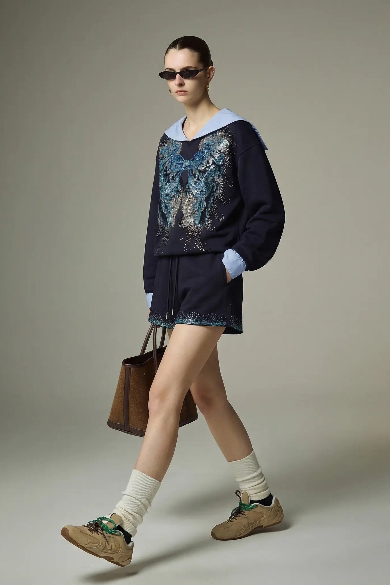 Model wearing a dark sweater with a blue pattern, shorts, and beige shoes, holding a brown handbag. TCH Navy Sailor Bow Wings Rhinestone Two-Piece Set