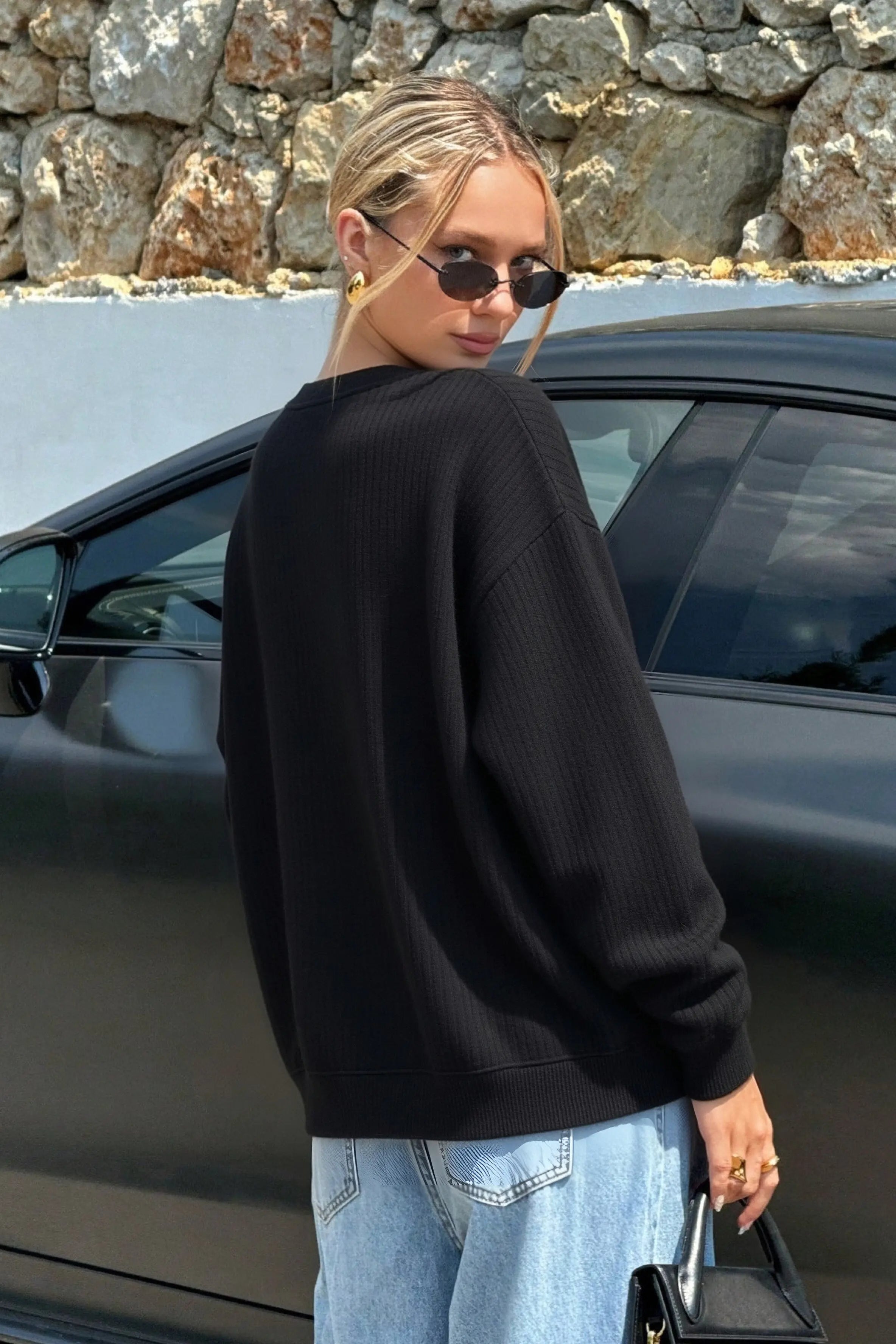 Woman in black sweater and jeans standing next to a black car with a stone wall background, TCH Peacock Embroidered Rhinestone Sweatshirt