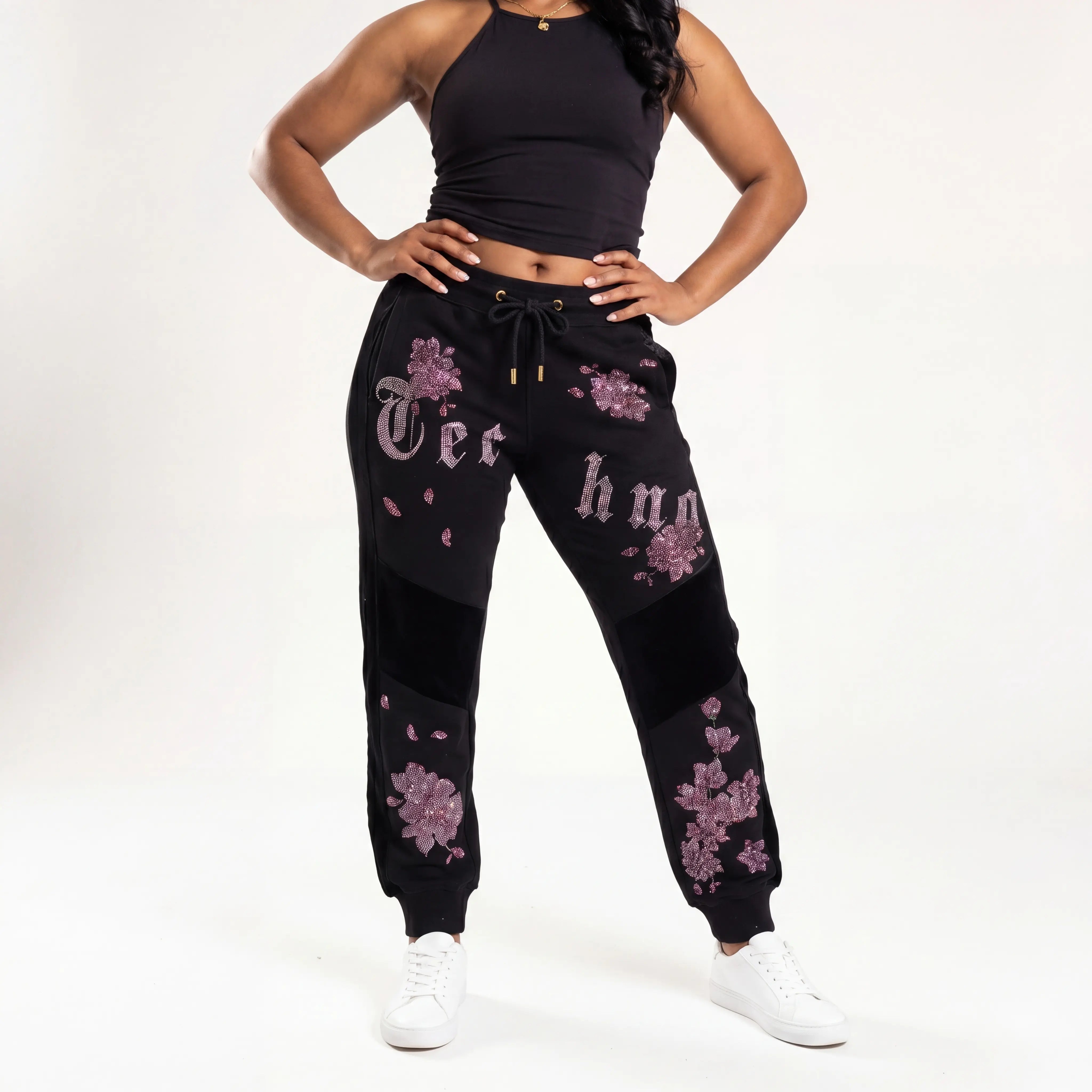 Person wearing black jogger pants with floral designs and text on a white background, TCH Pink Blossom Rhinestone Jogger Pants