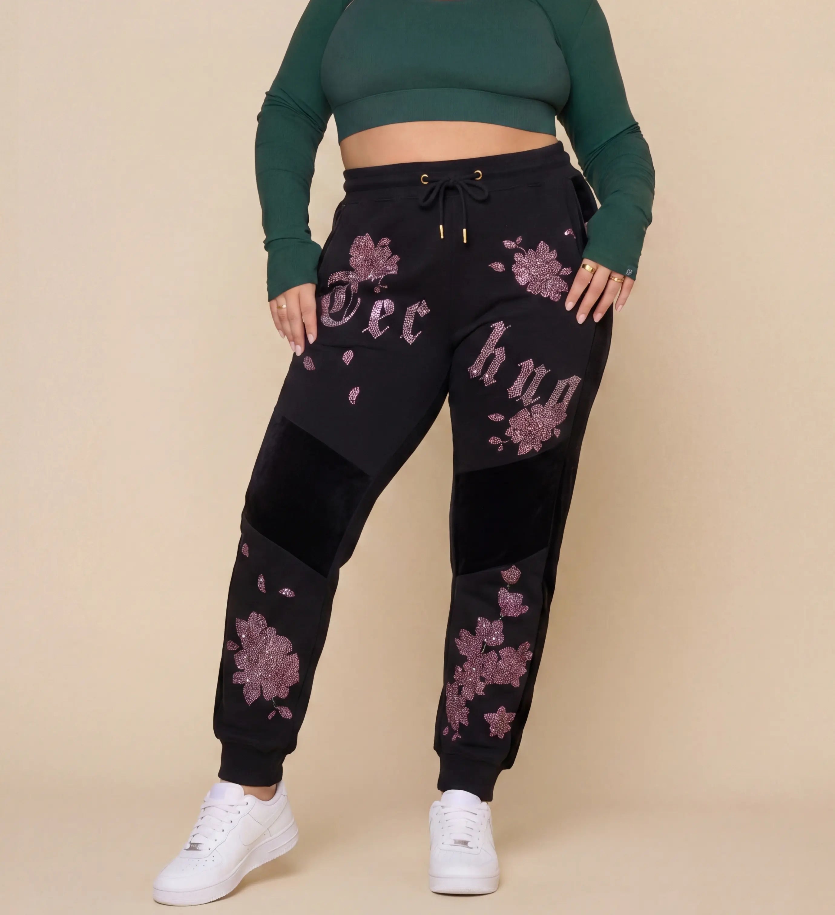 Person wearing black jogger pants with floral designs and a green crop top on a beige background, TCH Pink Blossom Rhinestone Jogger Pants
