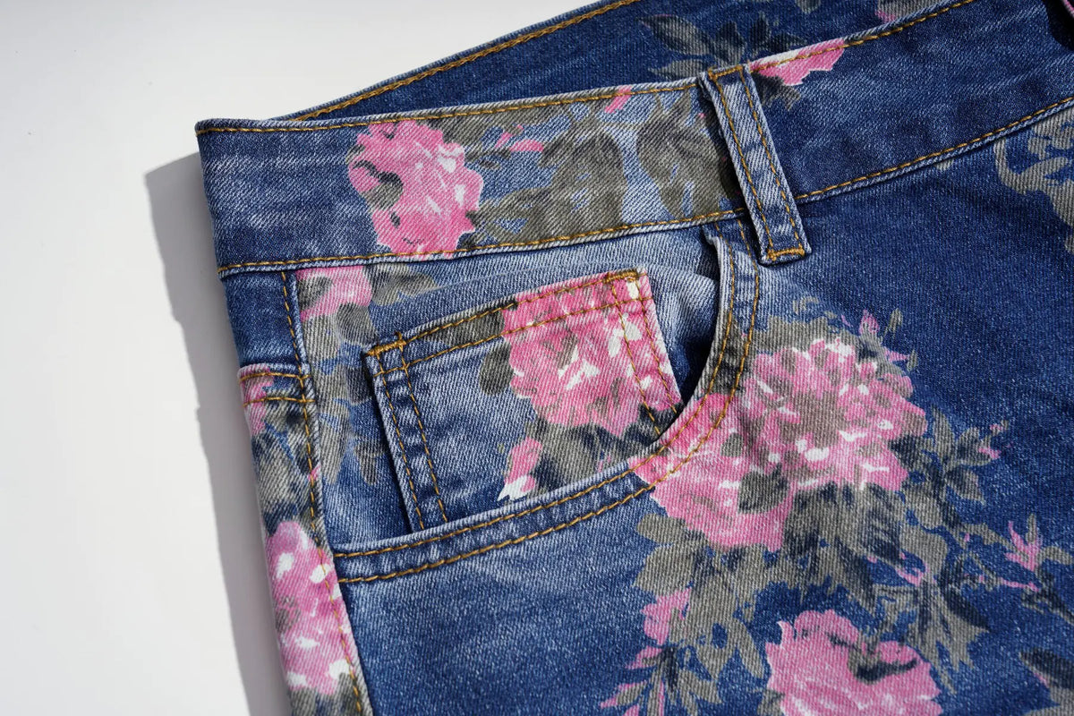 Close-up of a pair of blue denim jeans with a pink and gray floral print, showing the waistband, belt loop, and back pocket on a white background. TCH Pink Floral Teddy Bear Graphic Wide-Leg Jeans