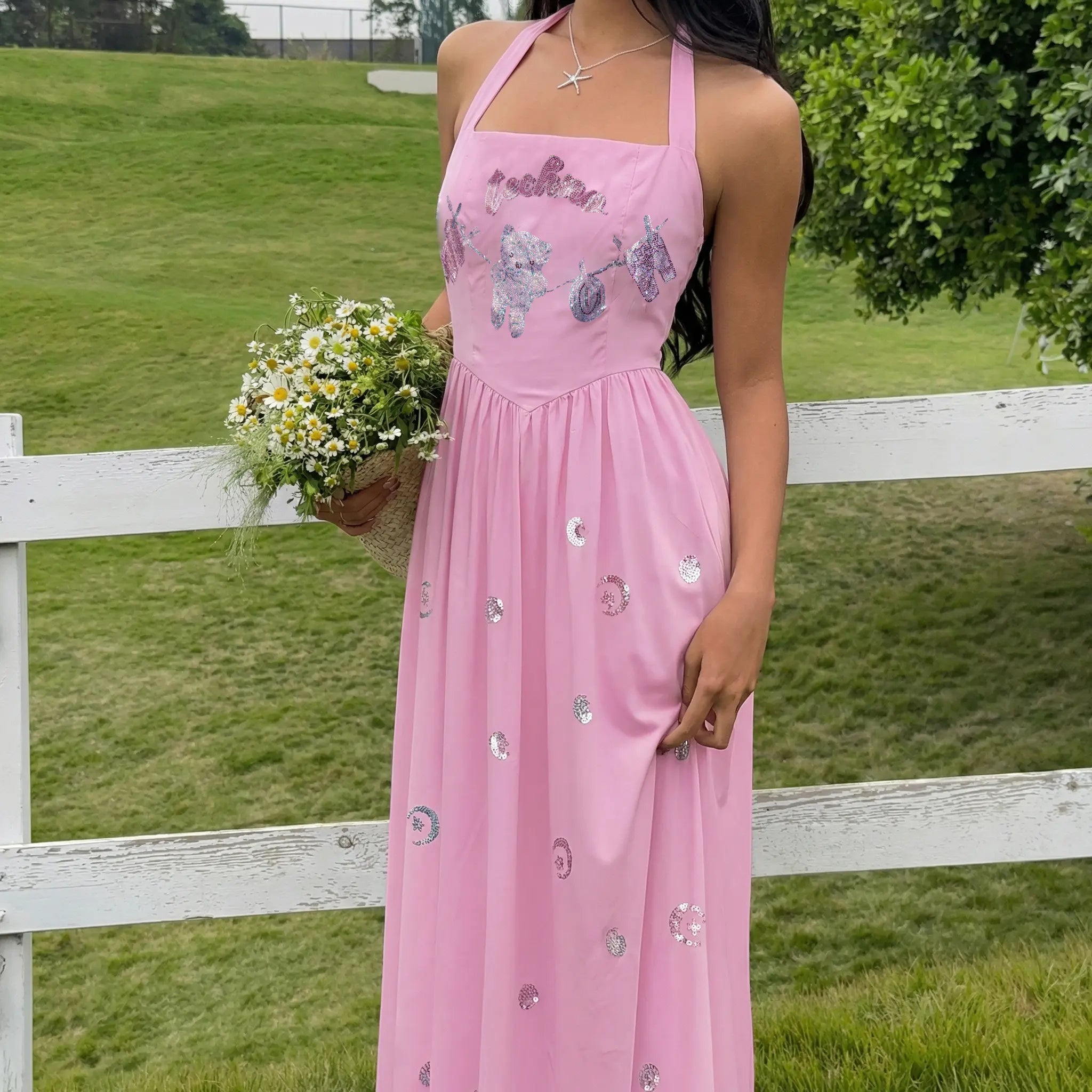 Woman in a pink dress holding flowers in a grassy field with a white fence. TCH Pink Rhinestone Teddy Laundry Story Dress