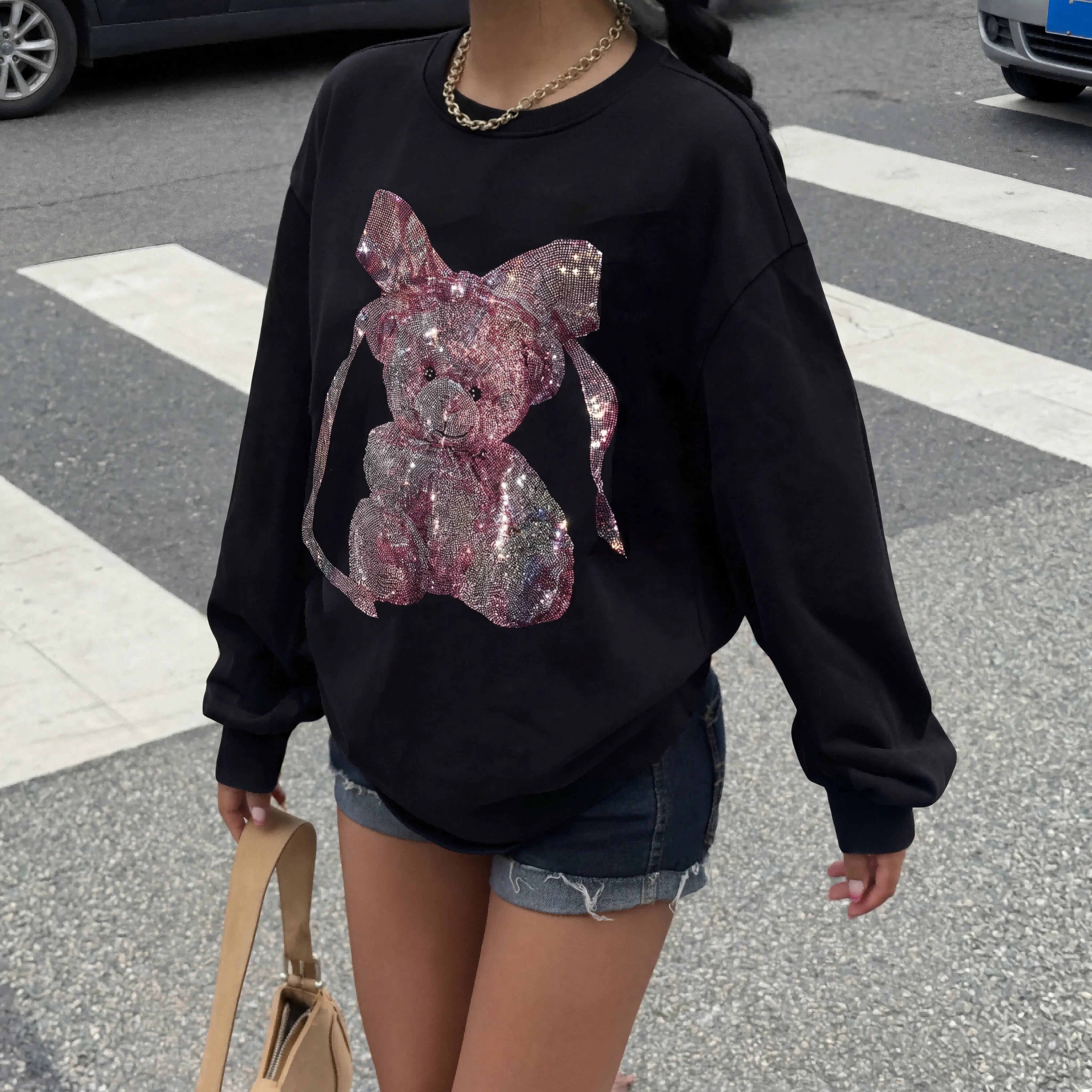 Person wearing a black sweatshirt with a pink sequin design on a street. TCH Pink Teddy Rhinestone Sweatshirt
