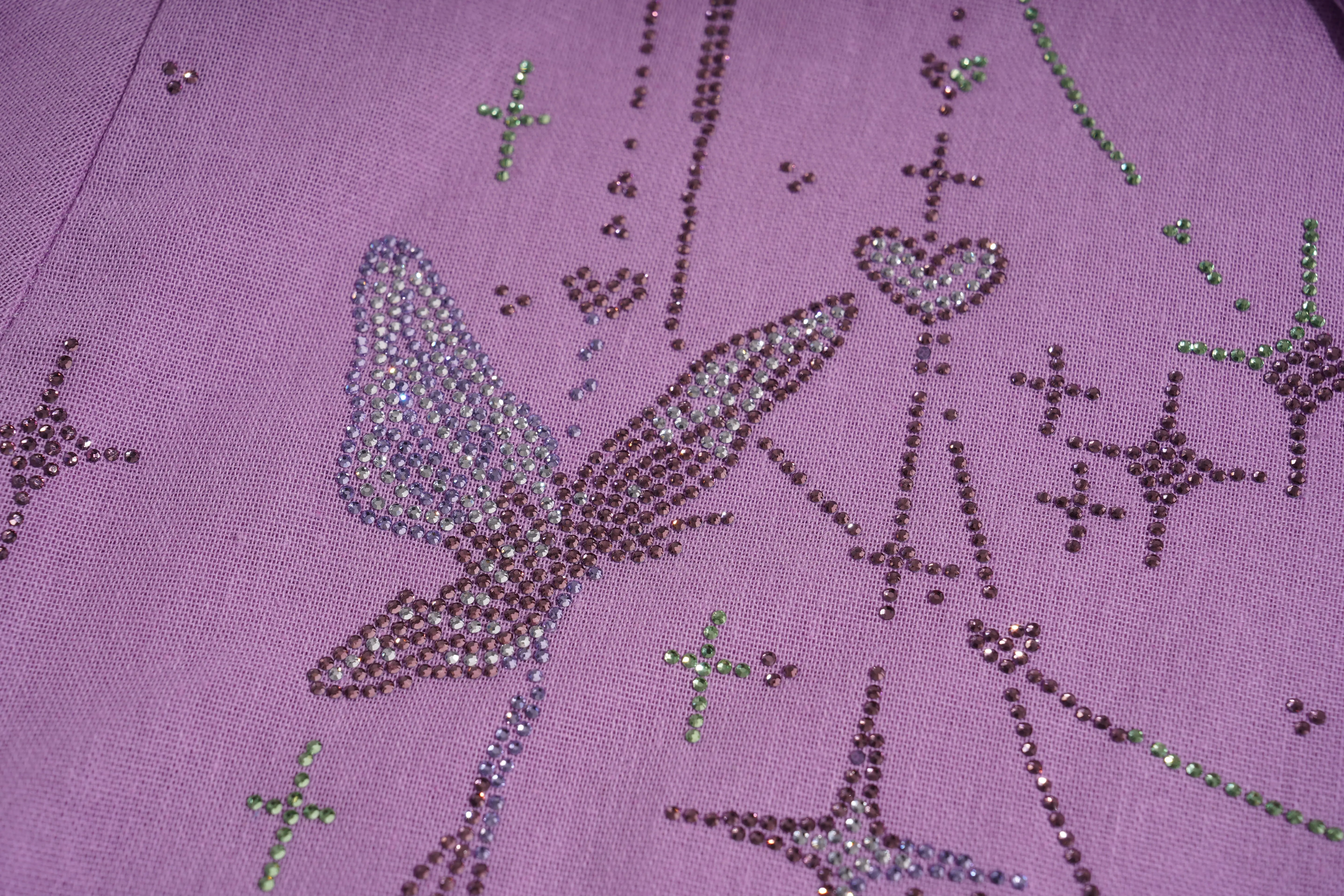Close-up of a purple fabric with decorative butterfly and star patterns. TCH Purple Rhinestone Butterfly Set