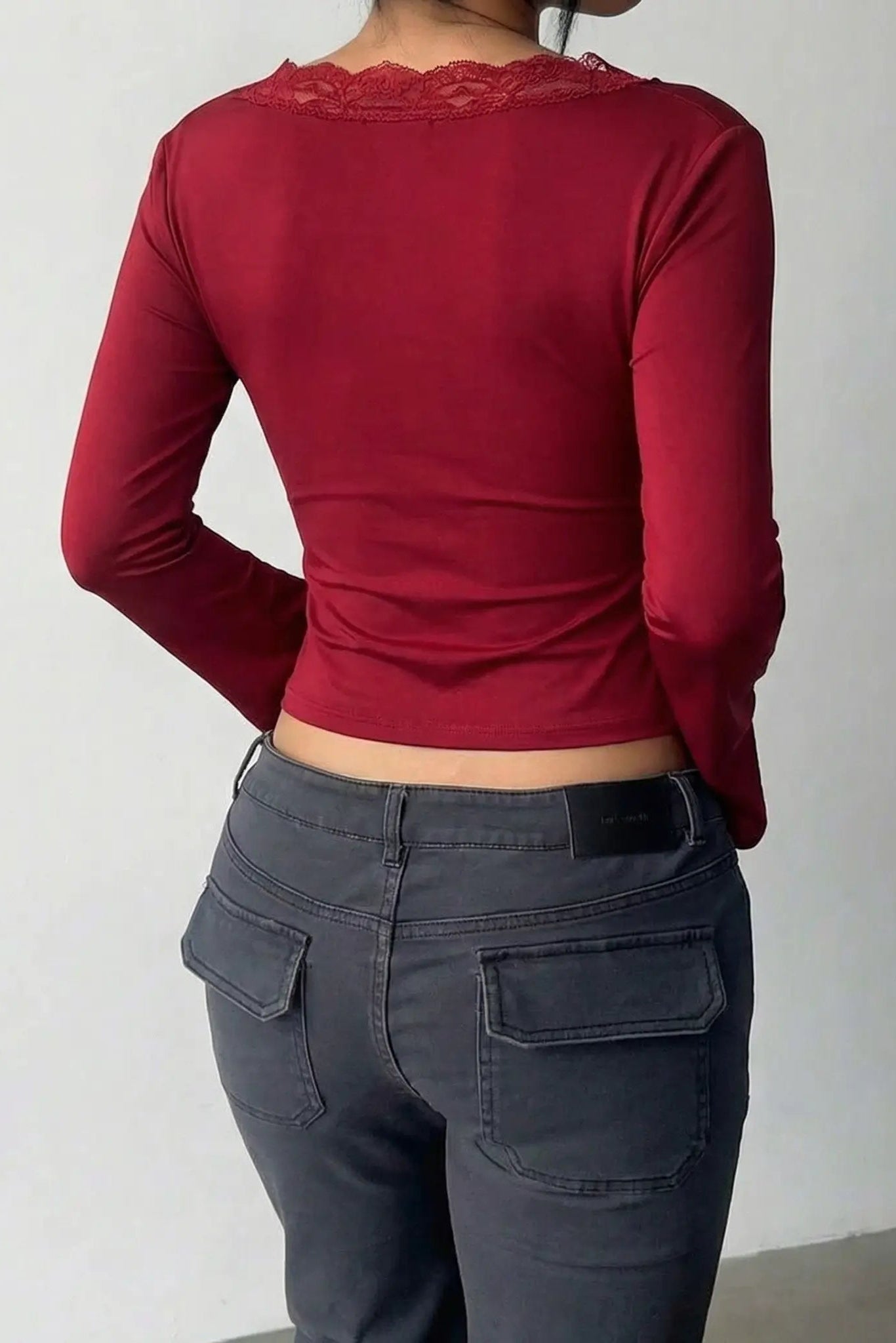 Person wearing a red long-sleeve top and dark gray pants against a plain background, TCH Red Lace Trim V-Neck Rhinestone Wing Long Sleeve Top