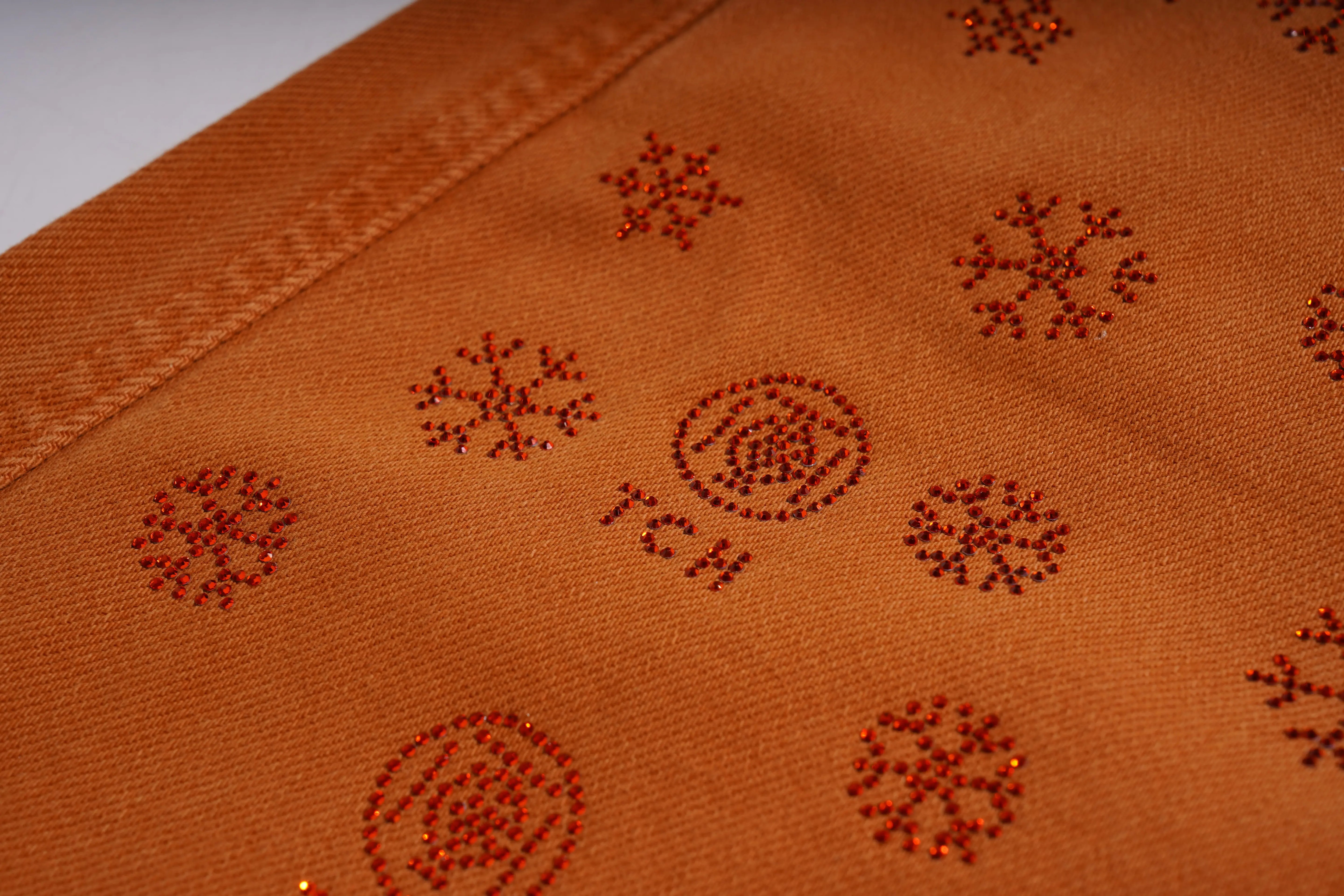 Close-up of a brown fabric with embroidered patterns on a plain background, TCH Red Snowflake Rhinestone Brown Denim Jeans