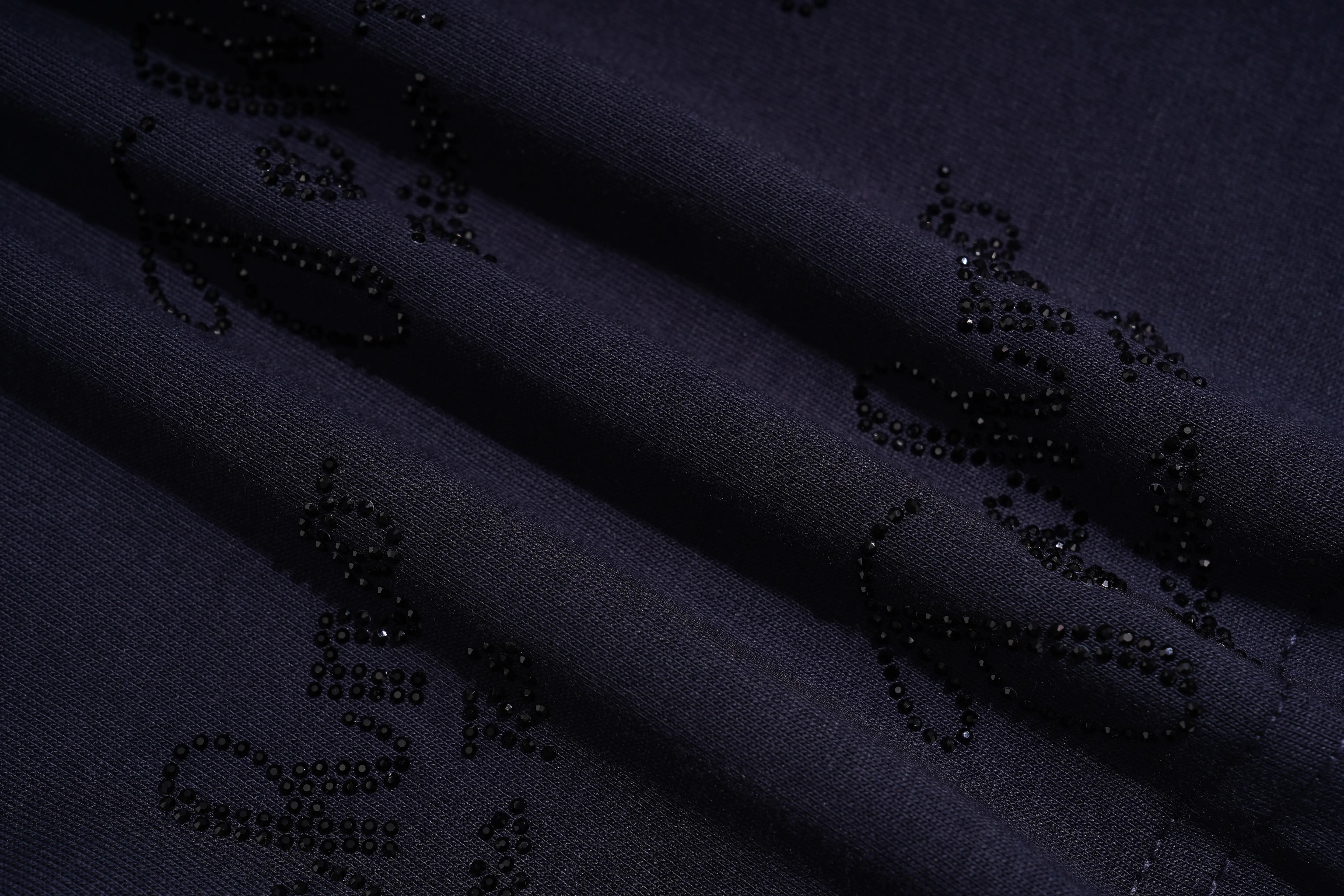 Close-up of a dark navy fabric with black beaded scrollwork patterns. TCH Rhinestone Angel Wing Gradient Cargo Shorts