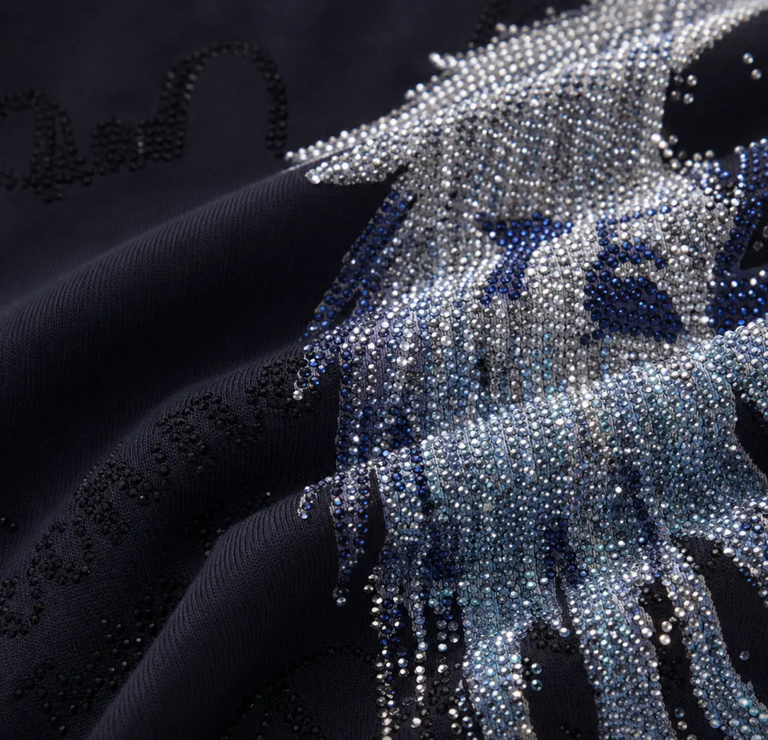 A close-up of a dark navy fabric with a detailed, textured beaded fringe design in silver, light blue, and deep blue tones. TCH Rhinestone Angel Wing Gradient Cargo Shorts