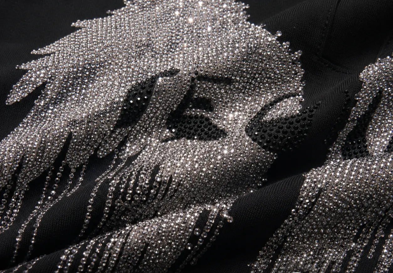 Close-up of a black garment heavily embellished with silver rhinestones, showing a large abstract graphic design and textured beaded details. TCH Rhinestone Angel Wing Graphic Shorts