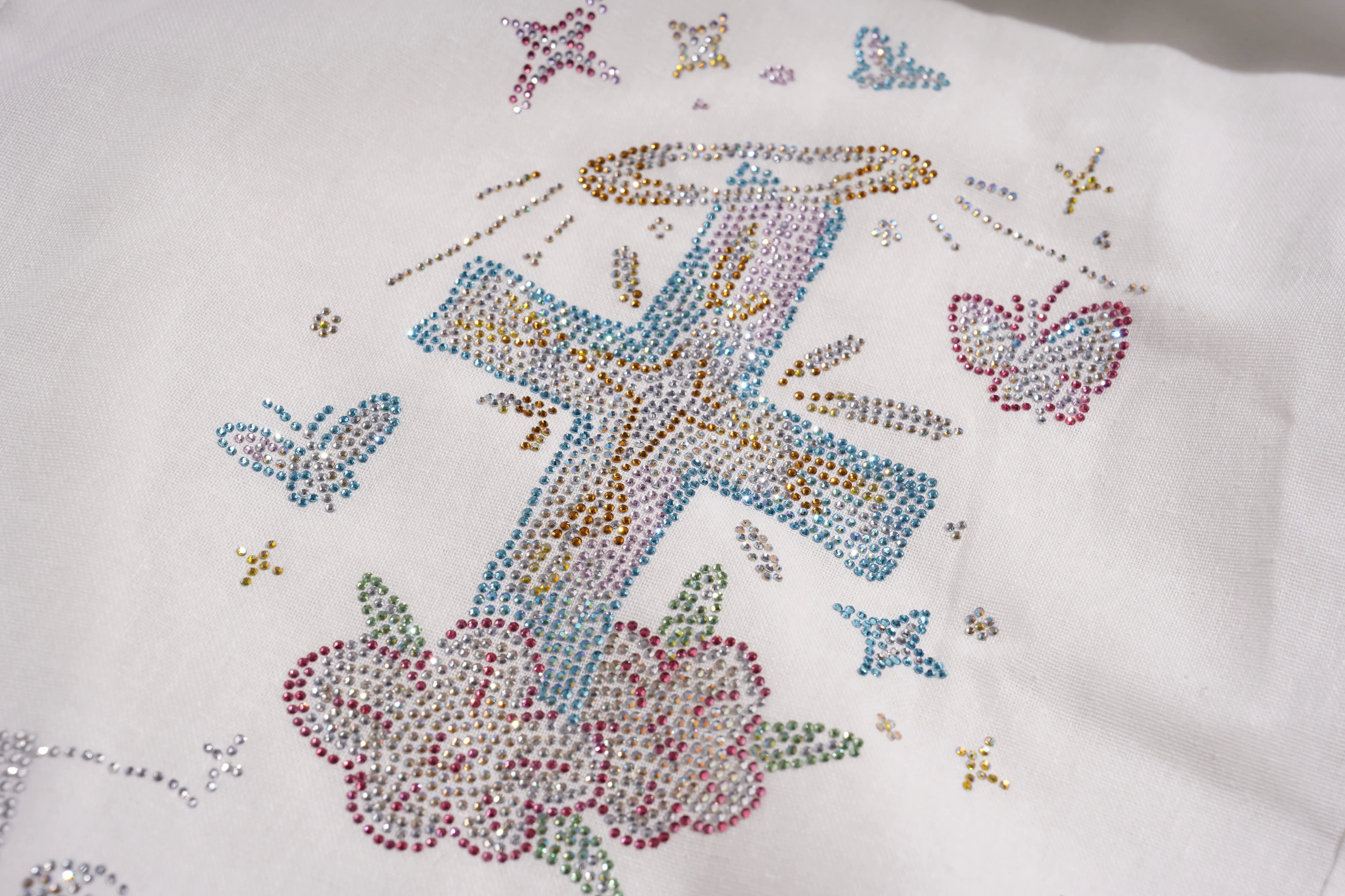 Embroidered design with a cross, flowers, and butterflies on a white fabric background. TCH Rhinestone Angel Wings & Cross Set