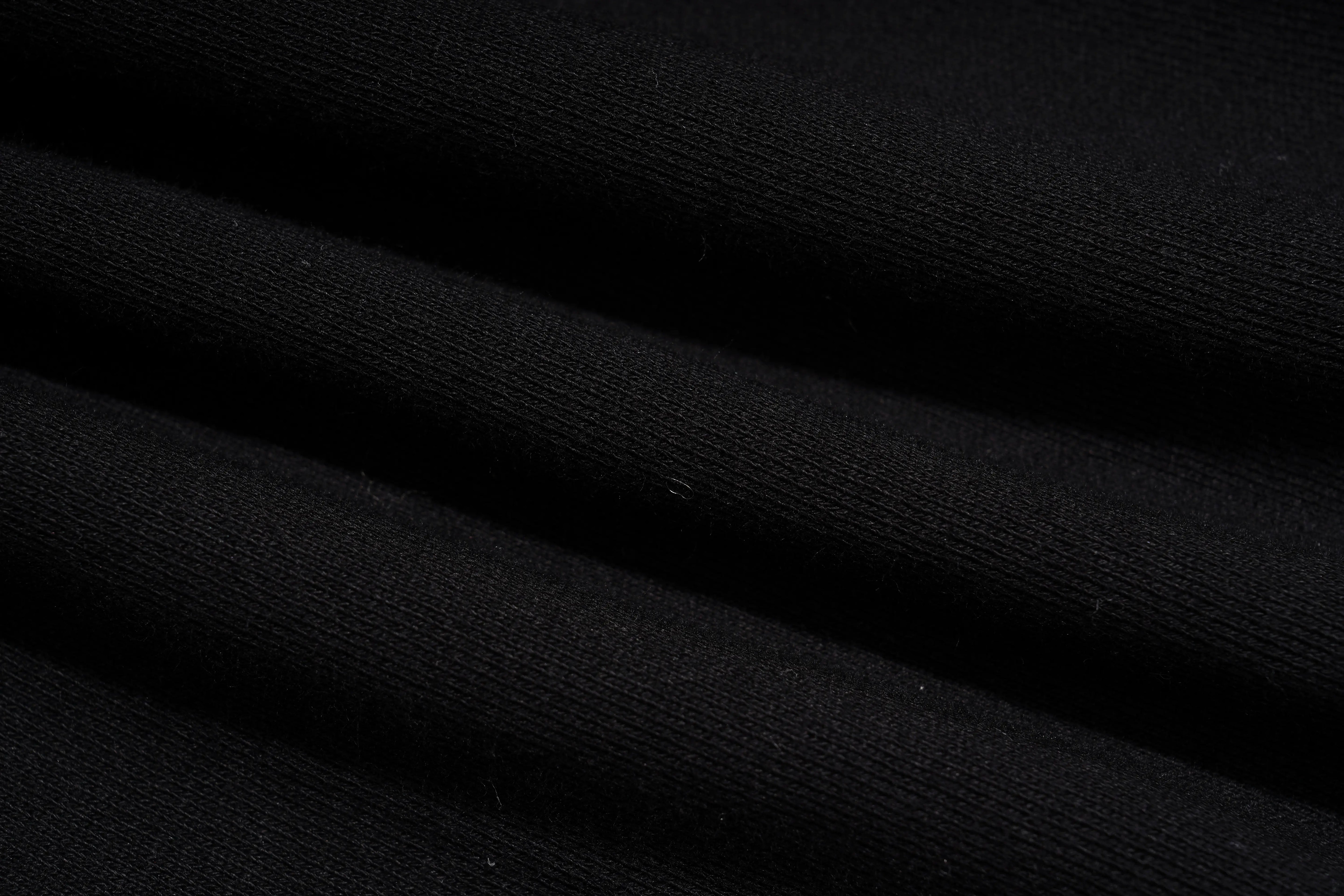 A close-up of black ribbed knit fabric with soft diagonal folds and visible fine texture. TCH Rhinestone Angel Wings Gold Detail Black Jogger Pants