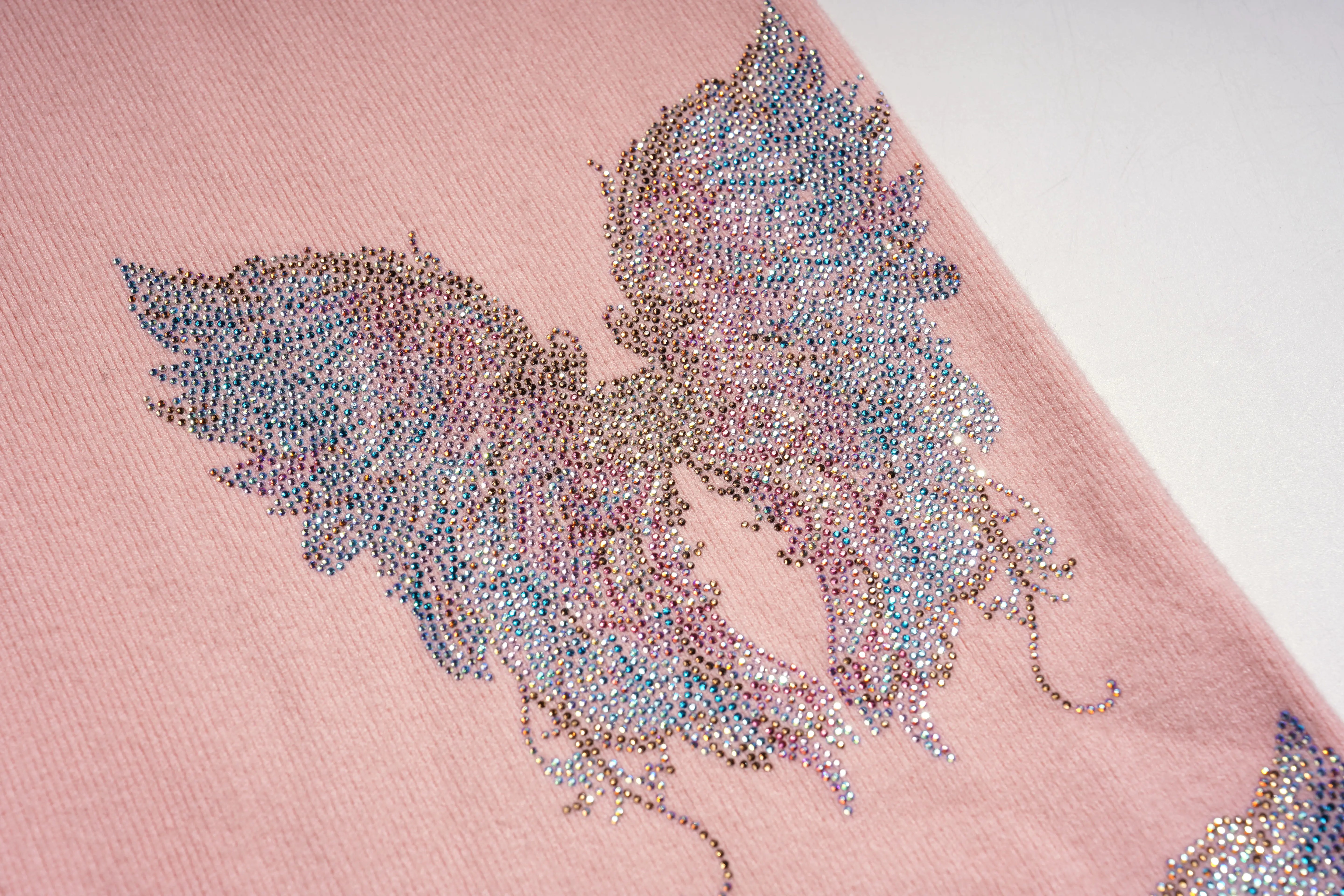 Close-up of a pink fabric with a decorative feather design made of small beads or crystals. TCH Rhinestone Angel Wings Layered Knit Top & Wide-Leg Pants Set