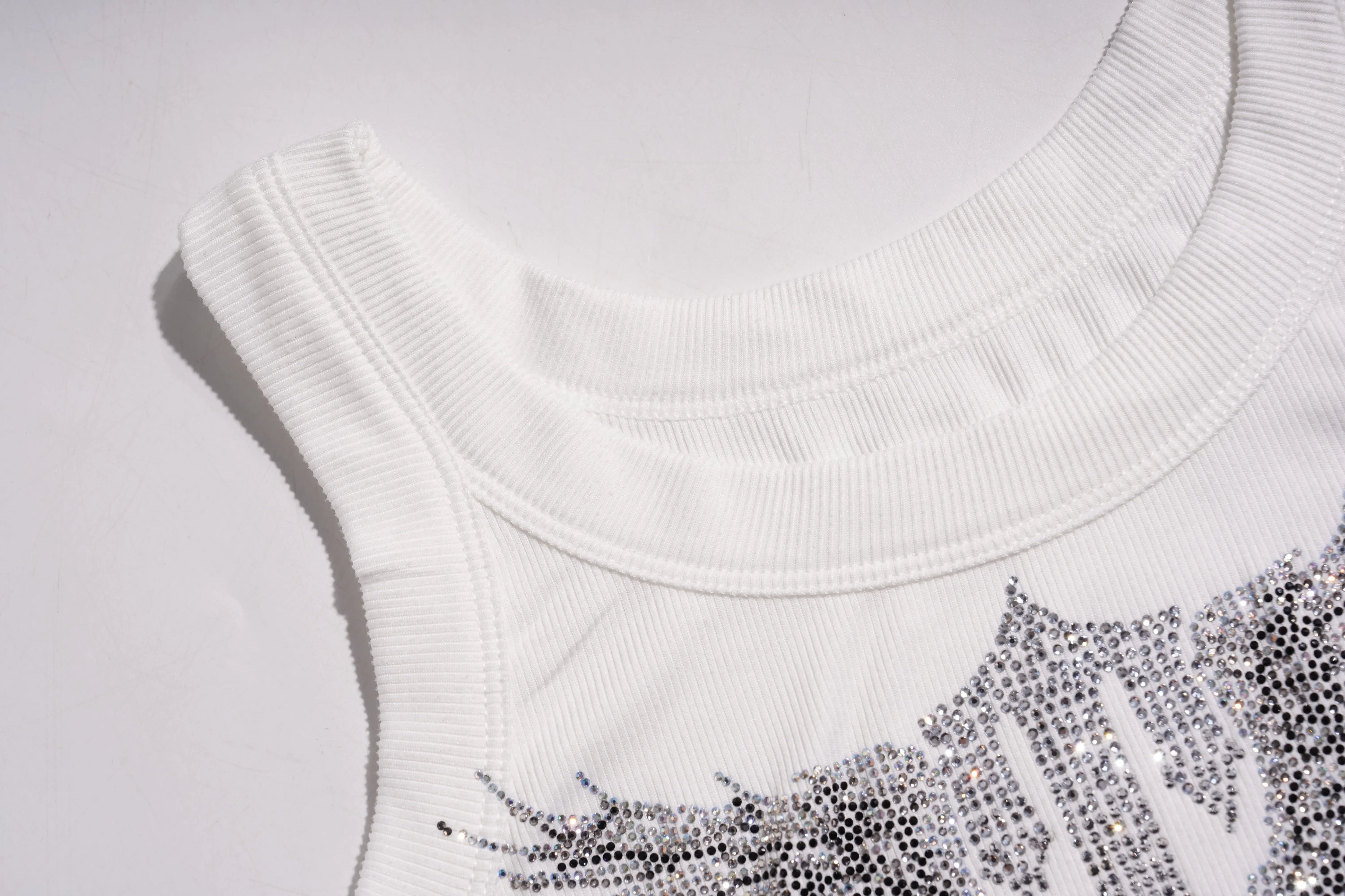 Close-up of a white sleeveless top with decorative elements on a light gray background, TCH Rhinestone Angel Wings Ribbed Tank Top