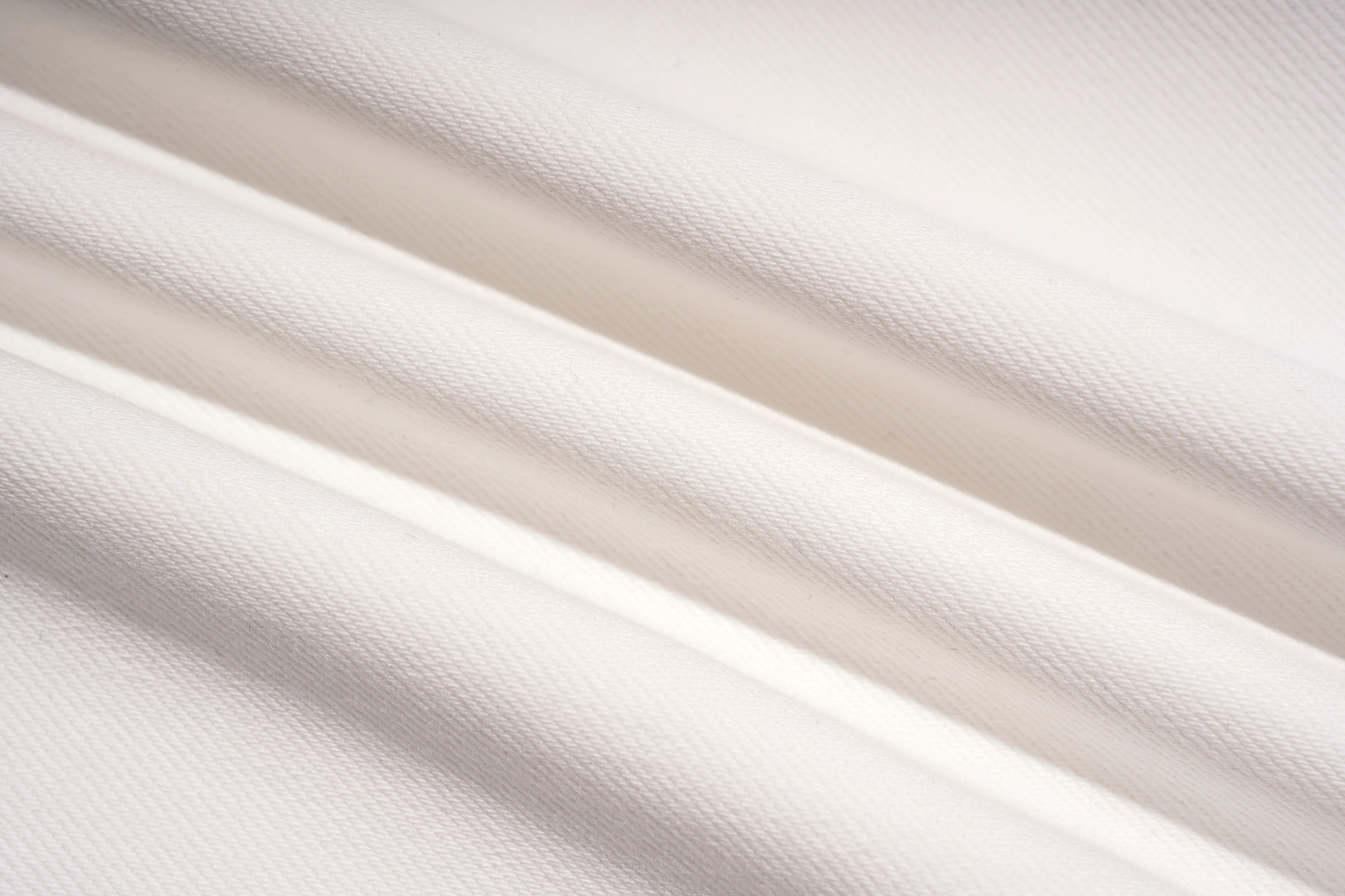 A close-up of draped white fabric with soft diagonal folds and a fine woven texture. TCH Rhinestone Angel Wings White Straight-Leg Jeans