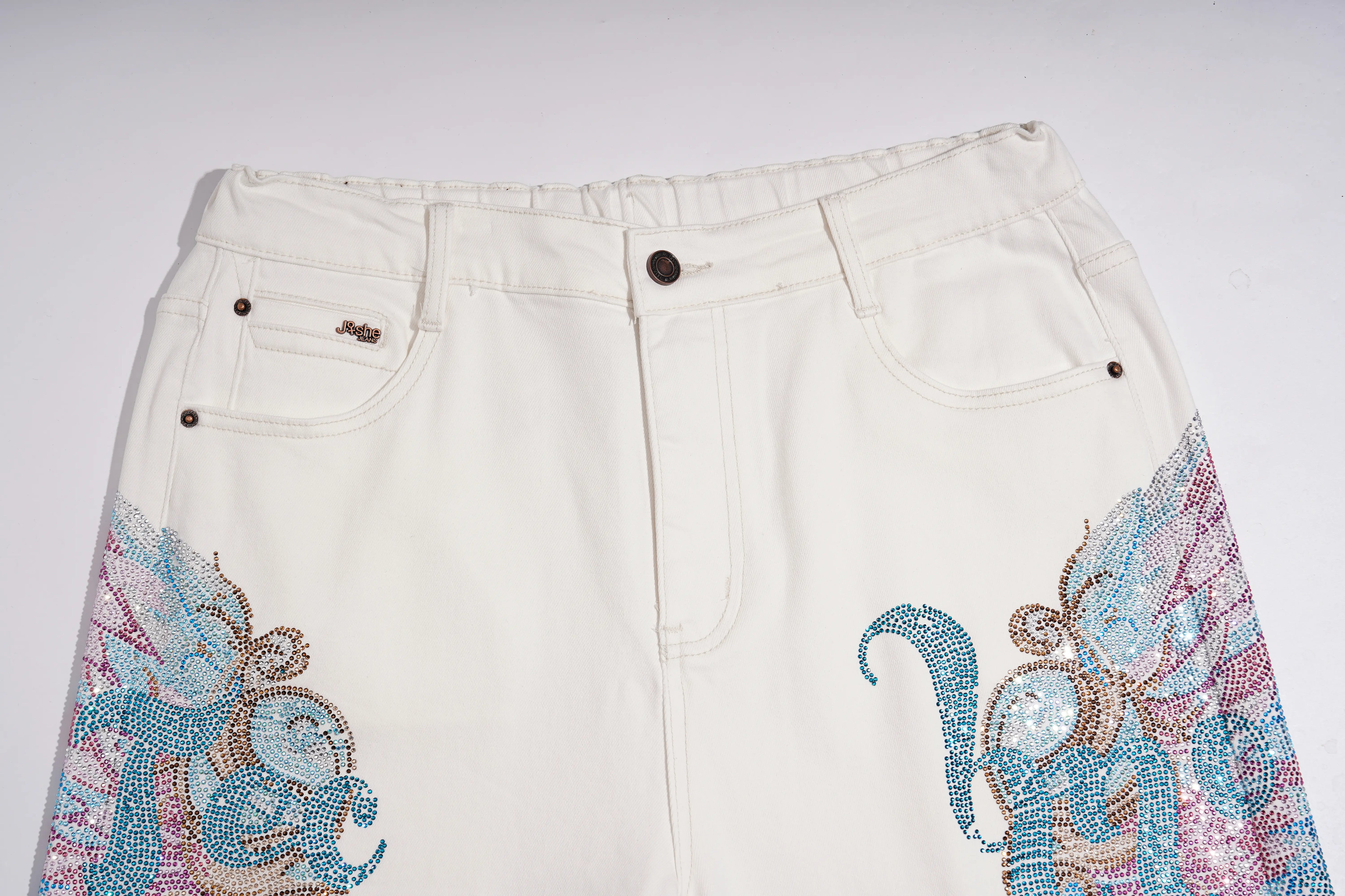 Off-white denim shorts featuring intricate rhinestone and beadwork embroidery in blue, pink, and gold on the lower left and right legs, shown against a plain light background. TCH Rhinestone Angel Wings White Straight-Leg Jeans