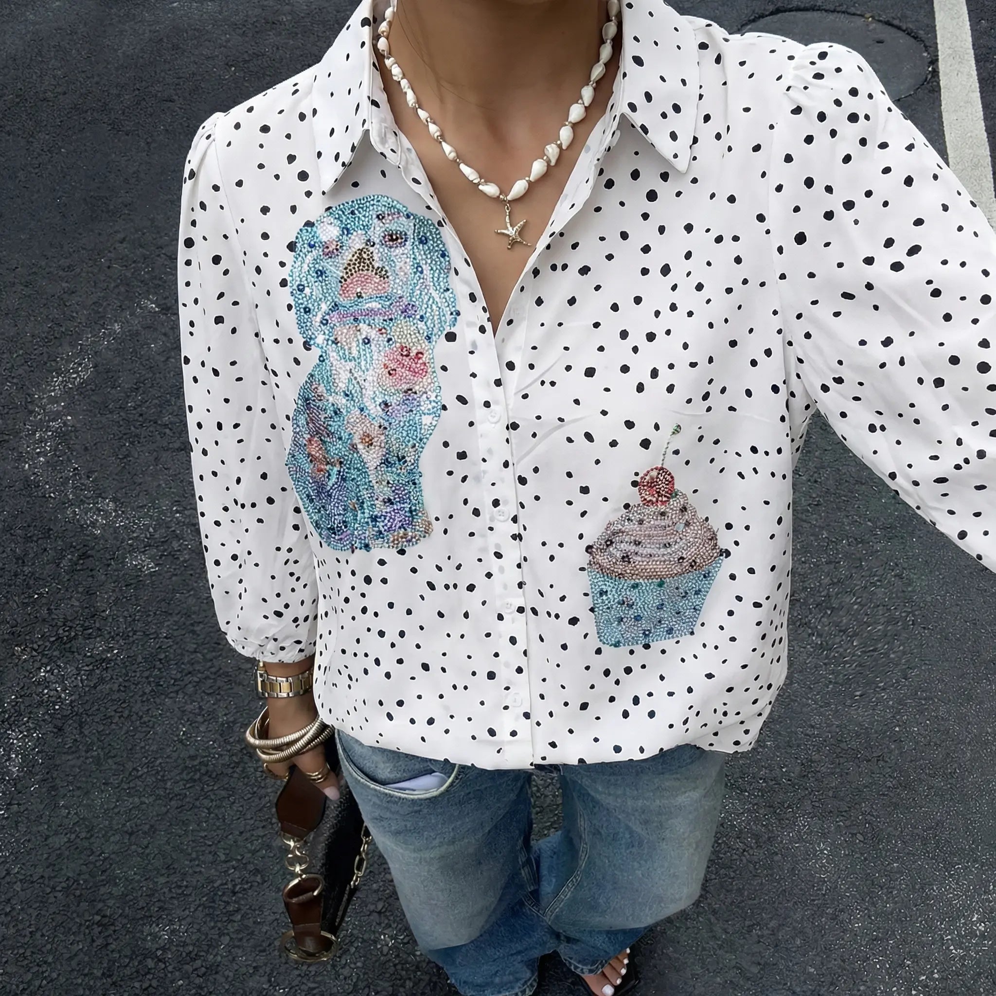 Person wearing a white polka dot shirt with colorful dog and cupcake designs, standing on a dark surface. TCH Rhinestone Animal Polka Dot Shirt