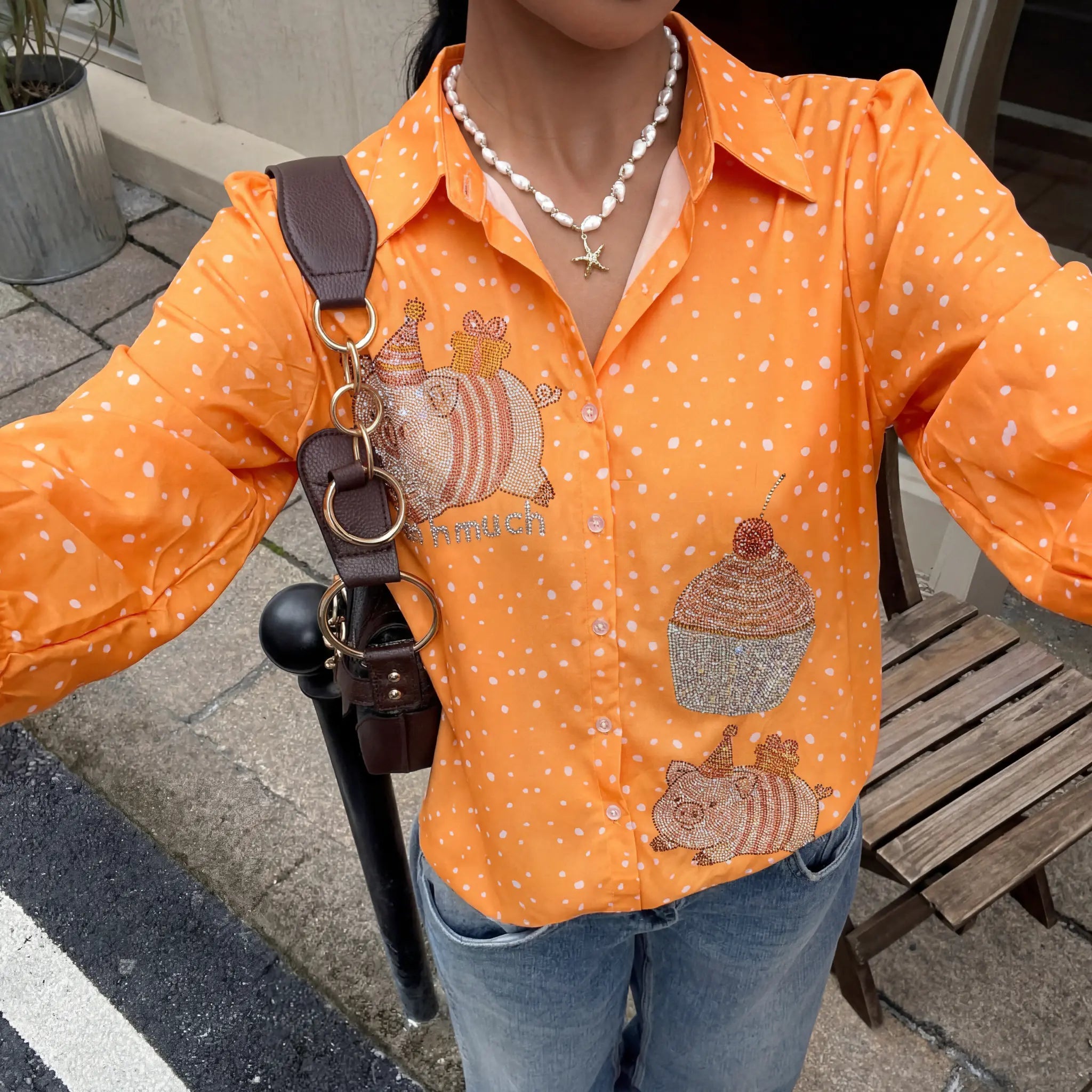 Person wearing an orange shirt with acorn designs, holding a brown bag with keychains. TCH Rhinestone Animal Polka Dot Shirt