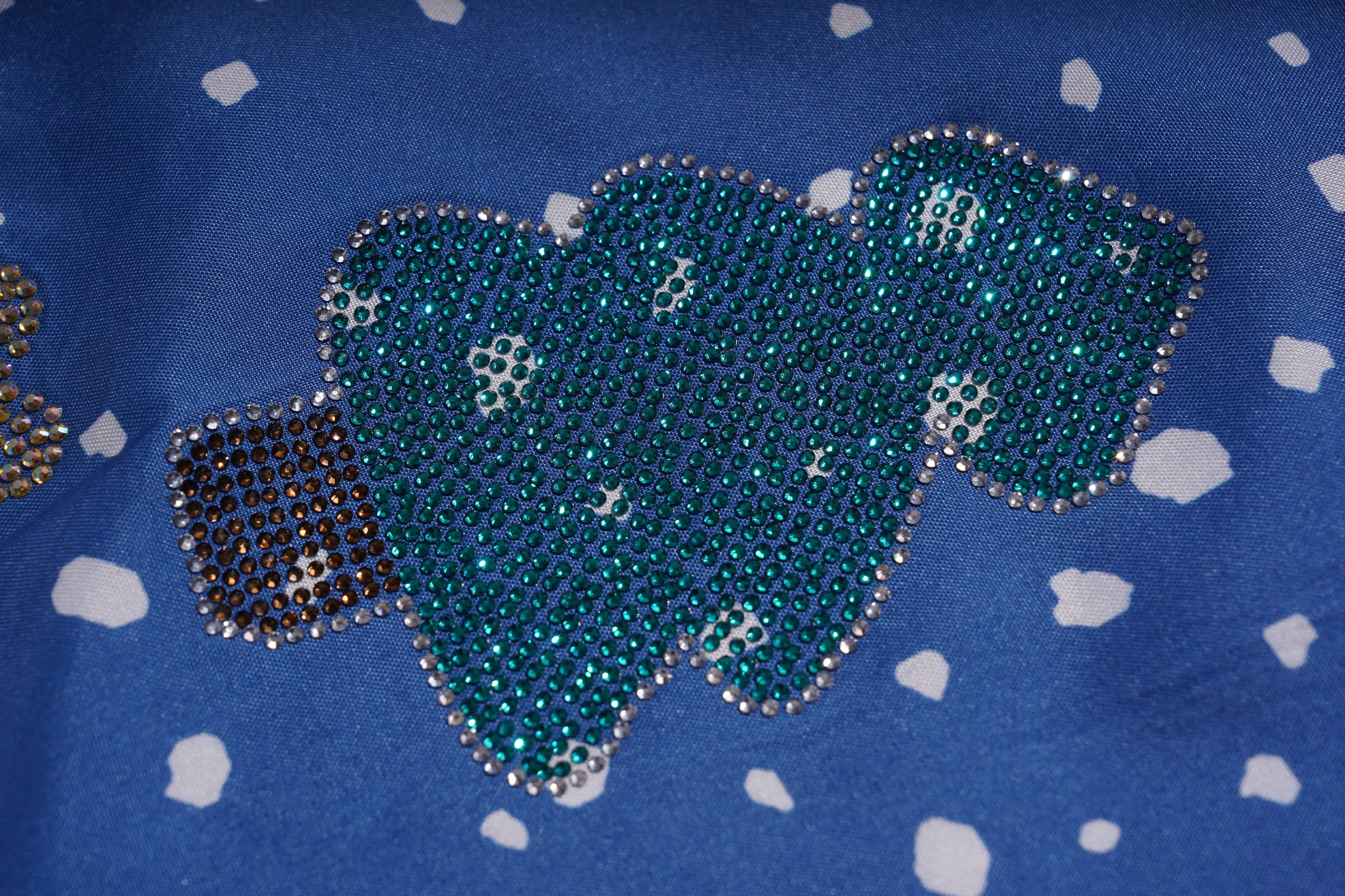 Decorative blue fabric with a heart-shaped embellishment on a blue background with white polka dots. TCH Rhinestone Animal Polka Dot Shirt