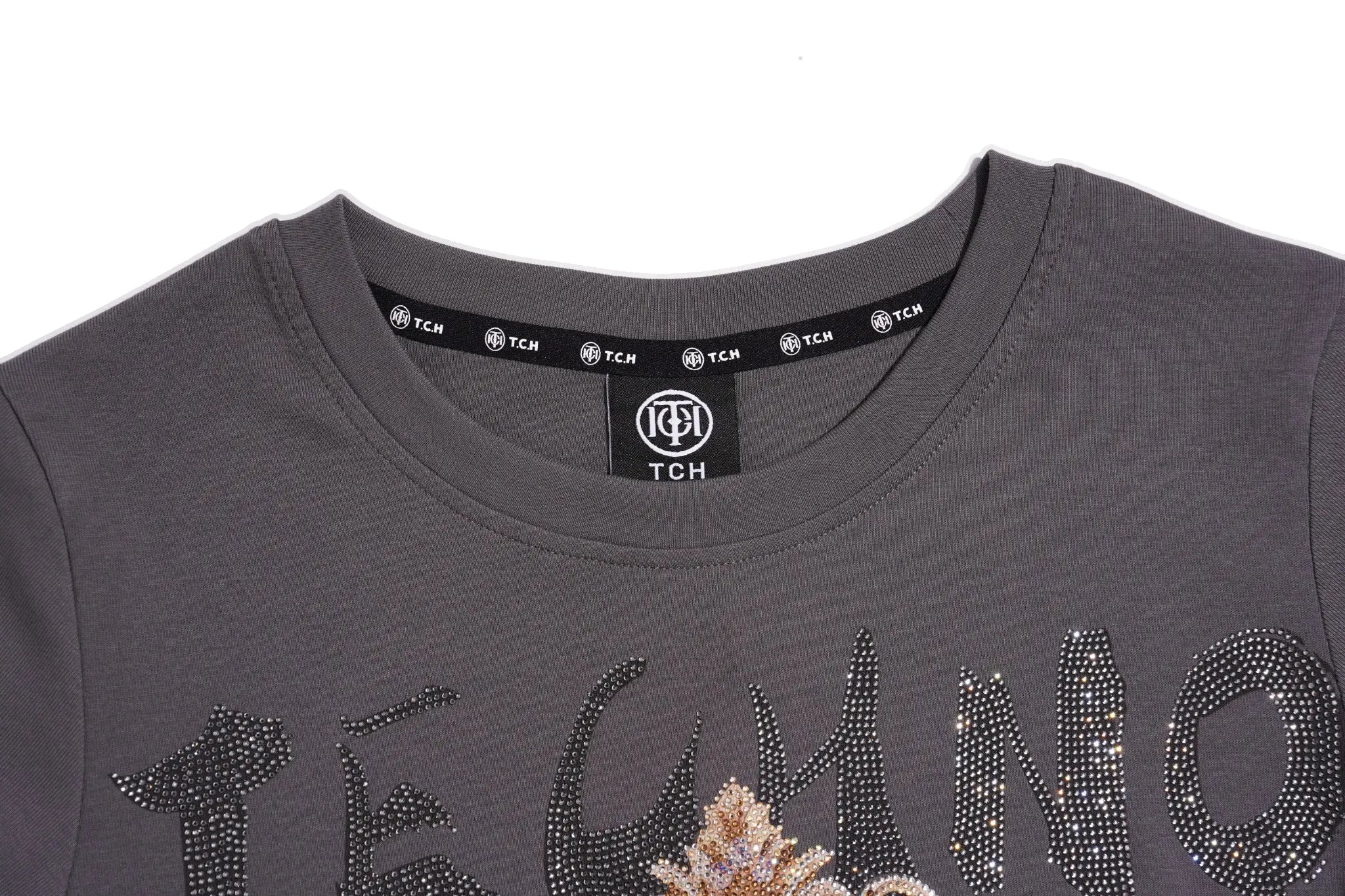 Close-up of a dark gray crewneck sweatshirt featuring a rhinestone-embellished graphic that spells 'TECHNO' across the chest, with a small floral embellishment in the center. The inner neck label shows the brand 'TCH'. TCH Rhinestone Bow Crown Graphic Mini Dress