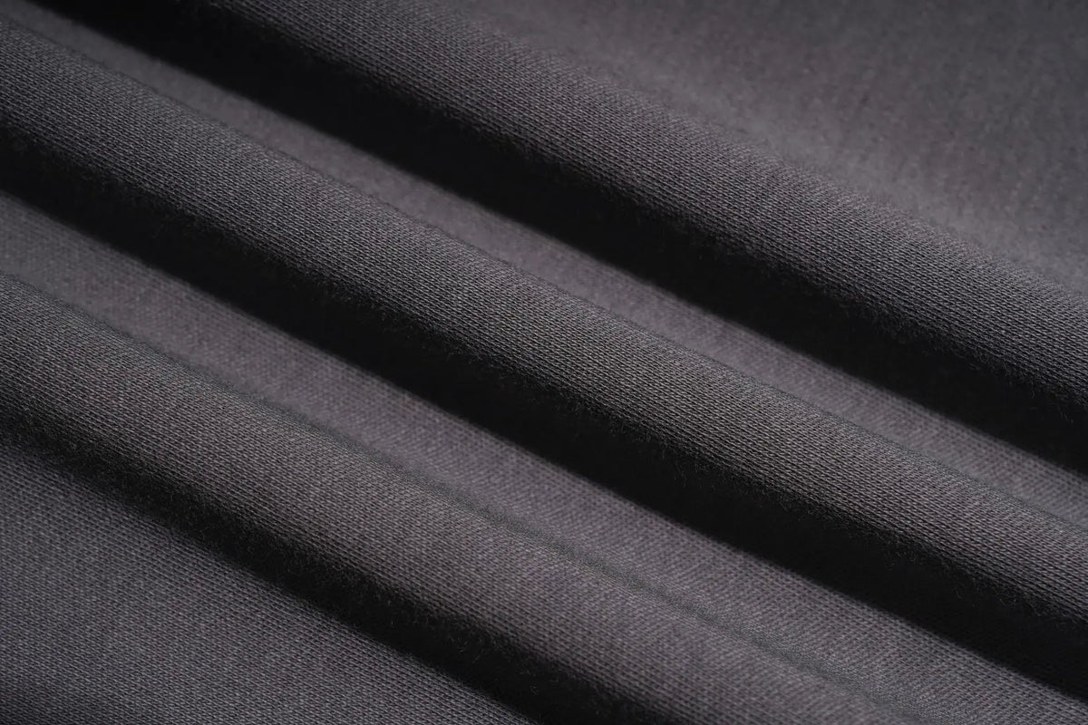 A close-up of dark charcoal gray fabric with soft diagonal folds showing a fine knit texture. TCH Rhinestone Bow Graphic Fitted Long Sleeve Top