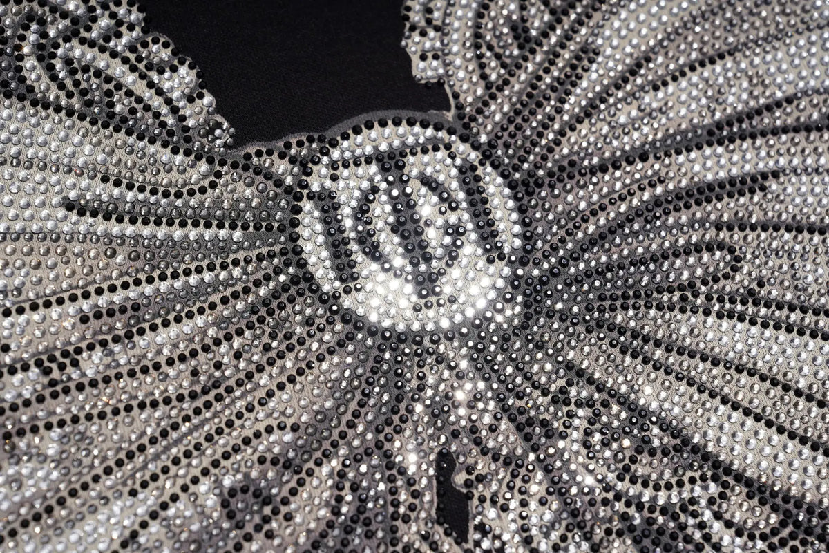 Close-up of a silver and black beaded embellishment with a central circular motif and radiating rows of rhinestones on a black background. TCH Rhinestone Bow Graphic Fitted Long Sleeve Top