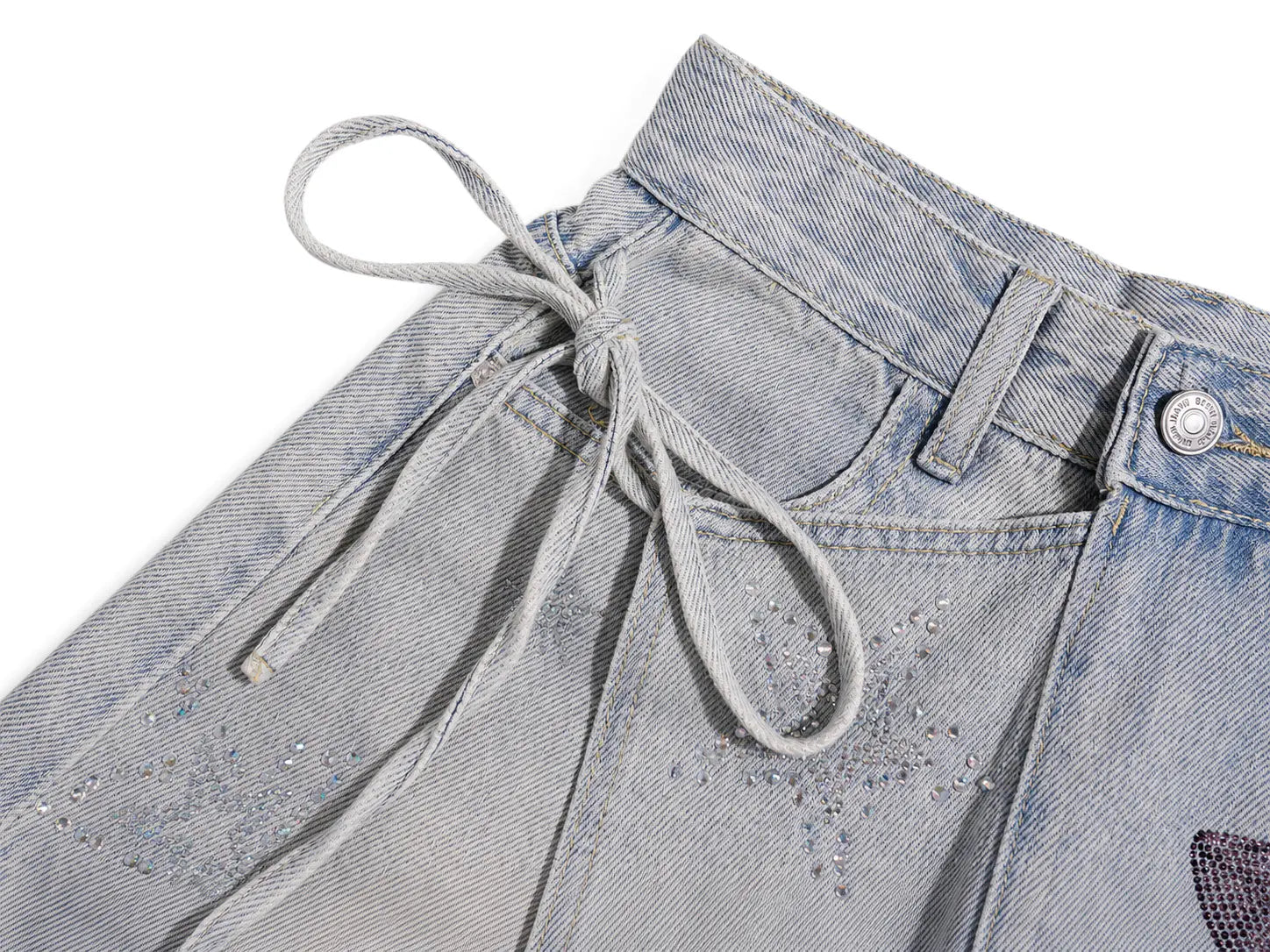 Close-up of a pair of light-wash denim shorts showing the waistband, drawstring tie, button closure, and textured fabric details on a white background. TCH Rhinestone Bow Light Wash Denim Shorts