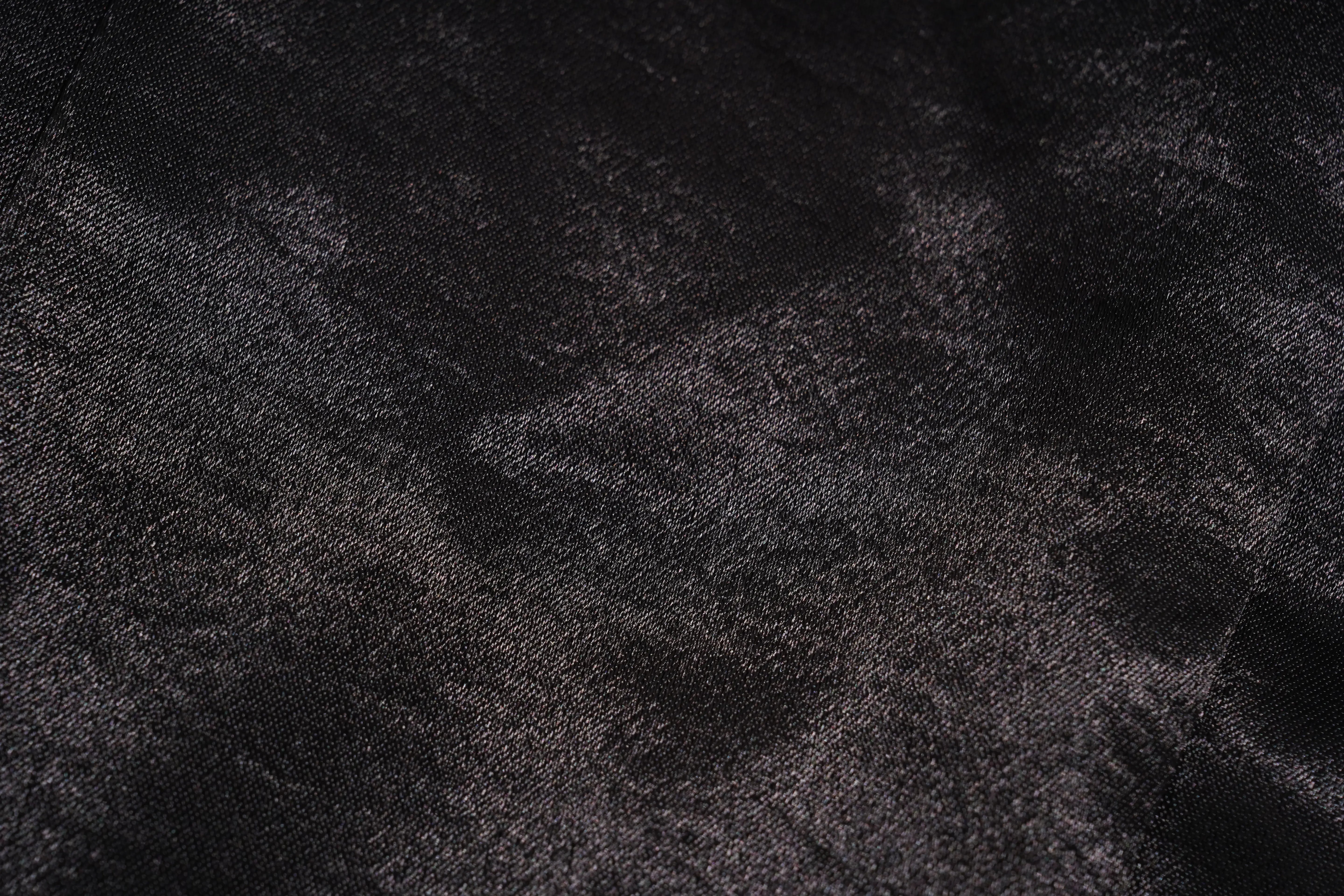 A close-up of a dark textured fabric with a subtle sheen, showing folds and a woven pattern in black and charcoal gray. TCH Rhinestone Bow Satin Blazer
