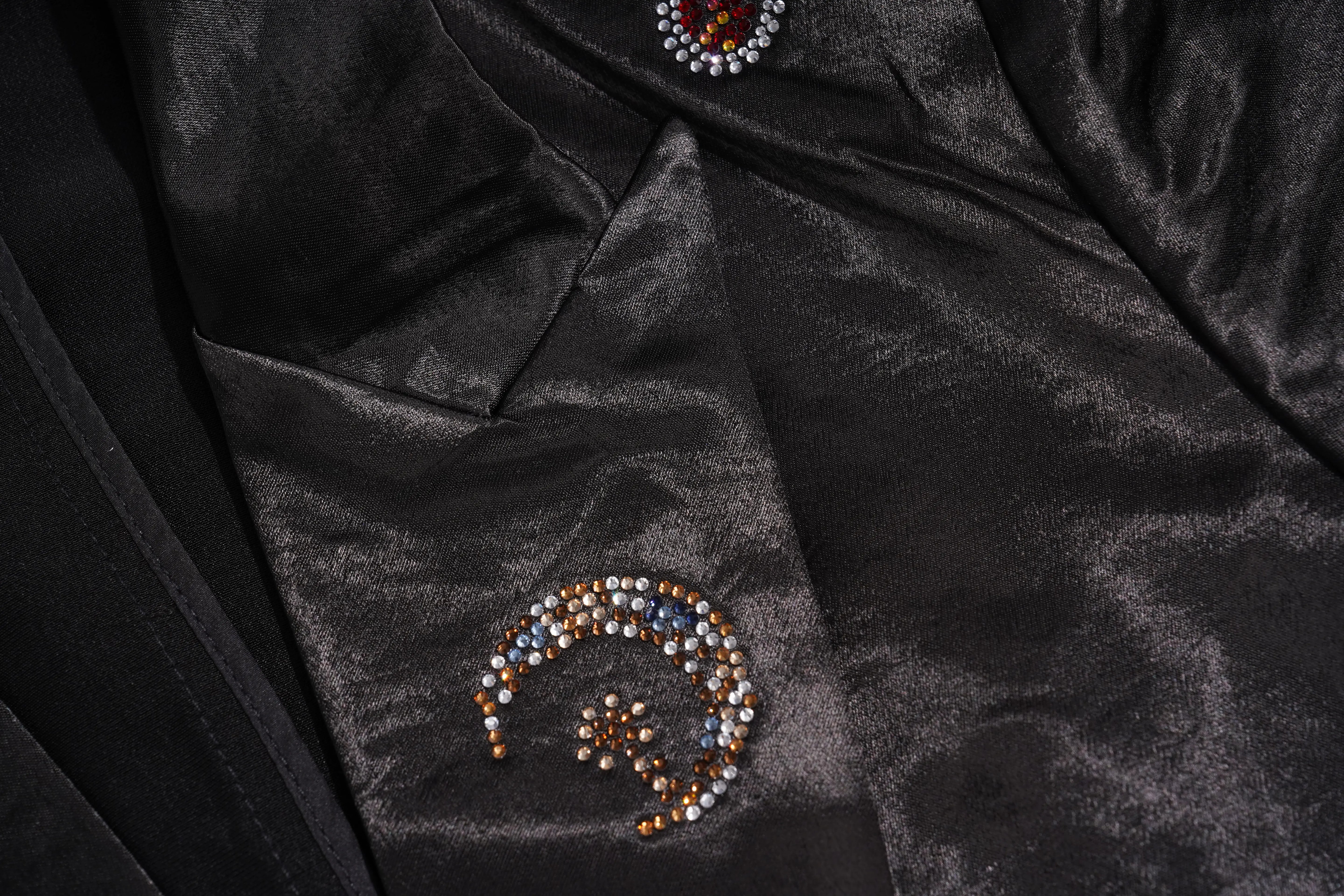 Close-up of a beige garment or fabric detail with decorative rhinestone embellishment along the top edge and a zigzag stitched seam on a white background. TCH Rhinestone Bow Satin Blazer