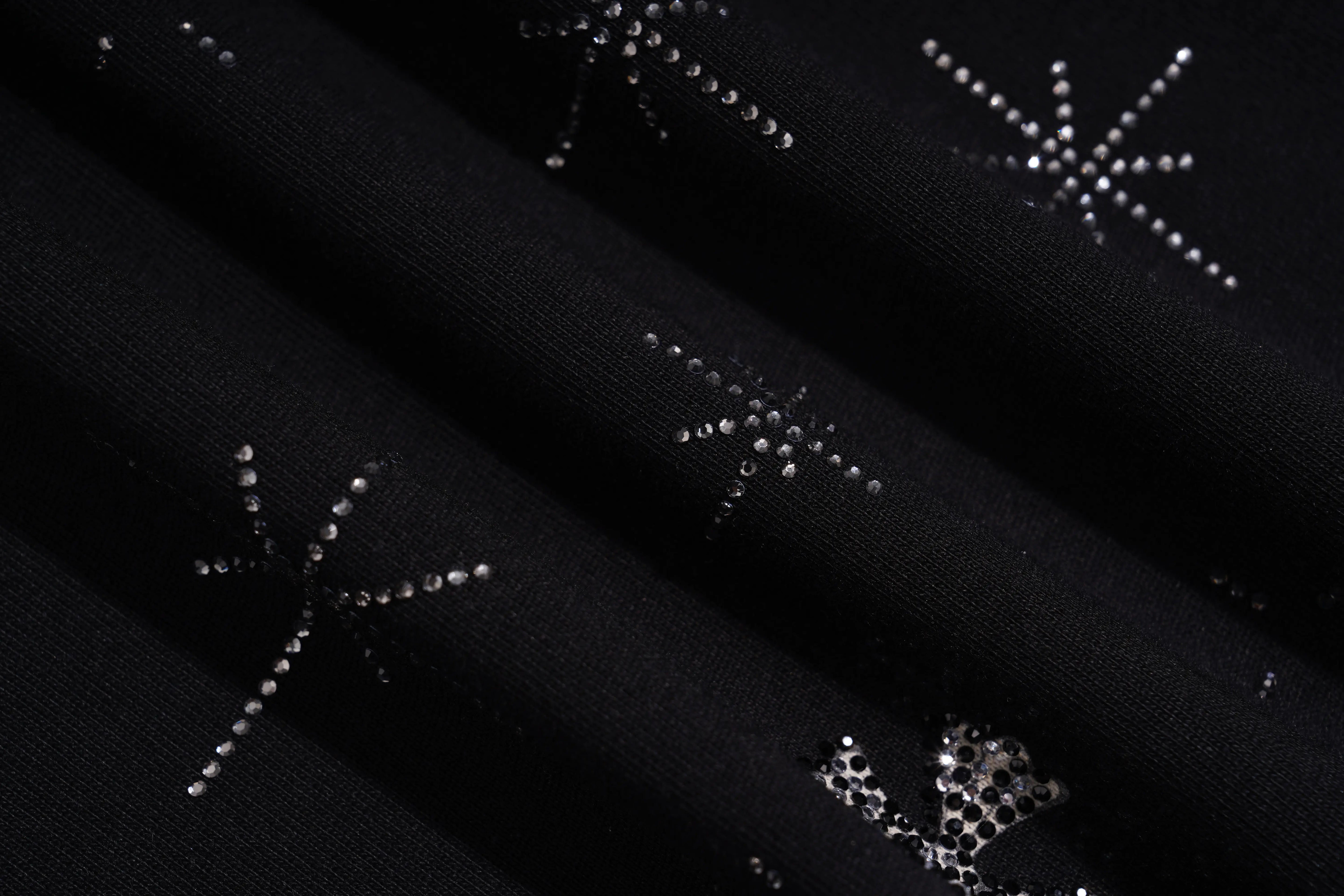Close-up of a black fabric surface with scattered silver rhinestone starburst embellishments. TCH Rhinestone Bow Star Pattern Black T-Shirt