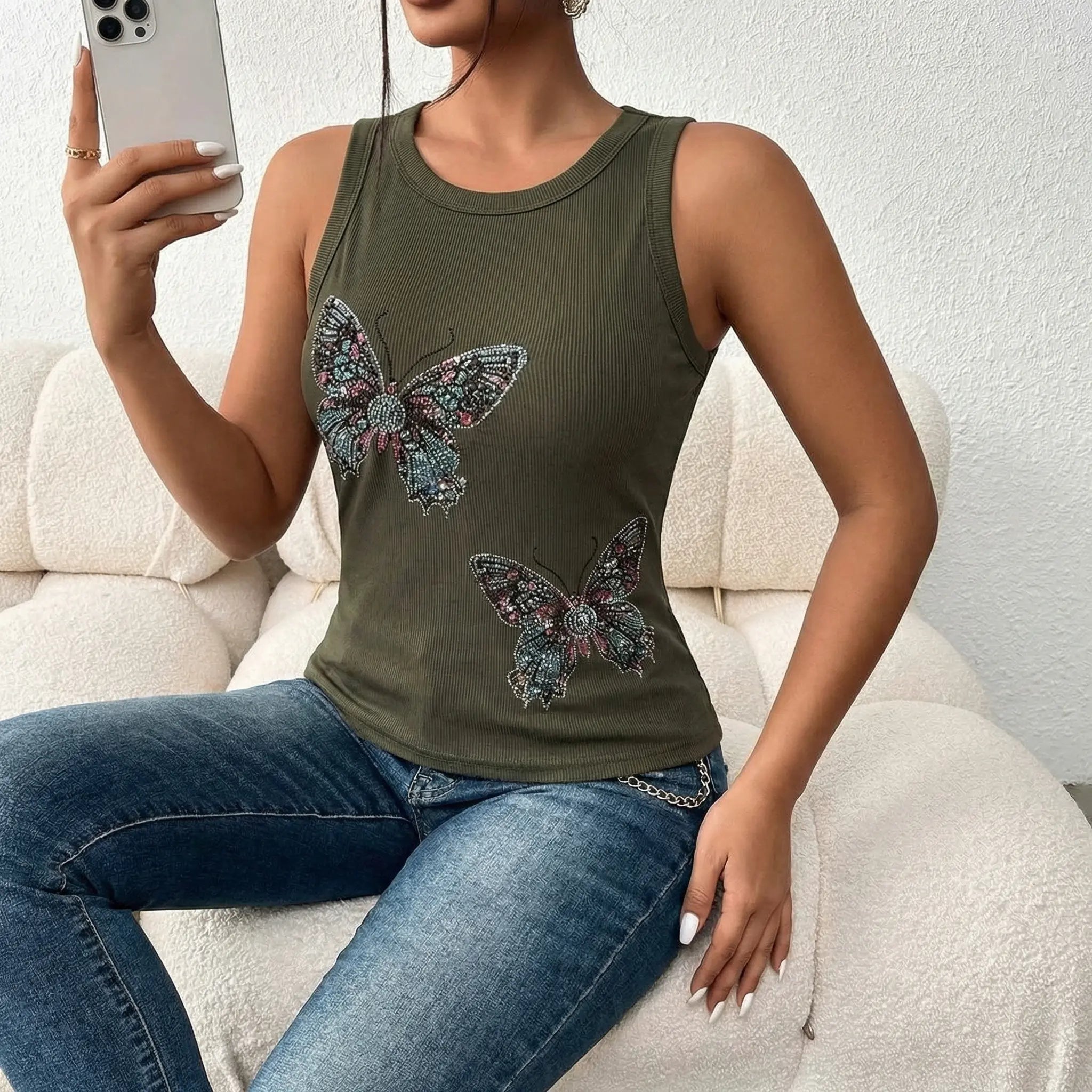 Woman wearing a green tank top with butterfly designs, sitting on a white couch. TCH Rhinestone Butterfly Bow Tank Top