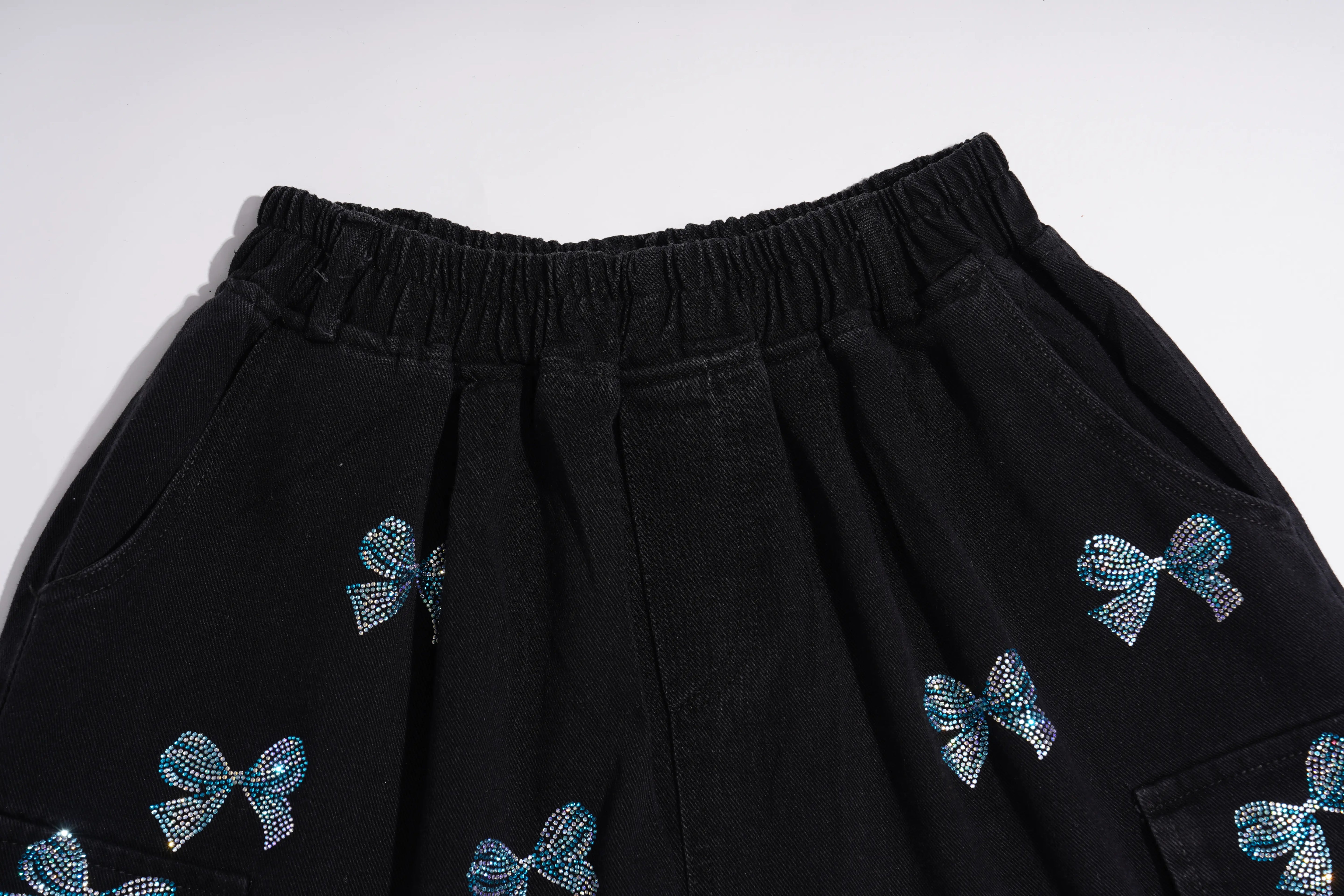 Black cargo-style shorts with an elastic waistband and small blue bow embellishments, shown against a plain light background. TCH Rhinestone Butterfly & Dragon Graphic Black Cargo Shorts