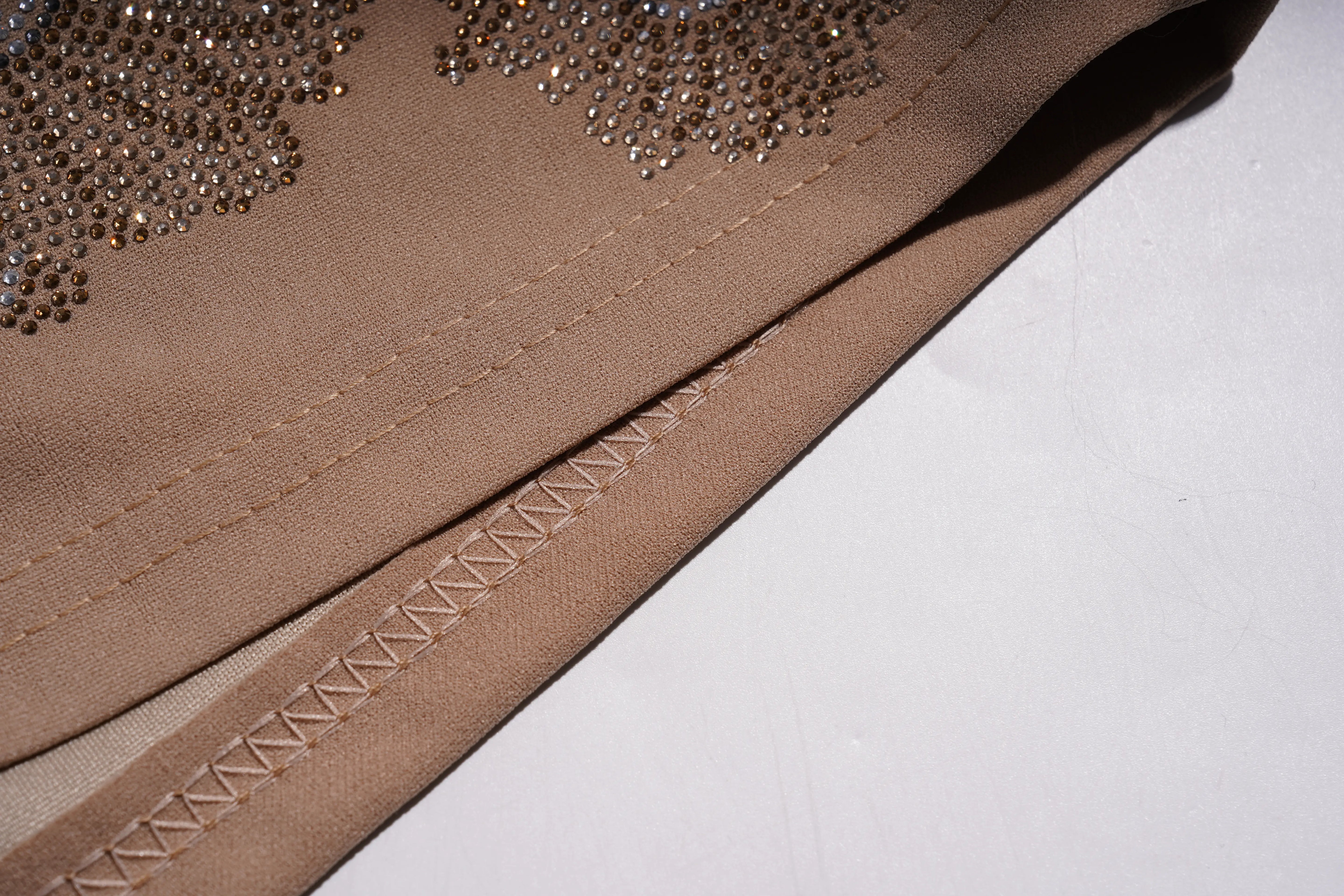 Close-up of a beige fabric garment or textile with decorative rhinestone embellishment along the top edge and a visible zigzag stitched seam on a white surface. TCH Rhinestone Butterfly Floral Embellished Tailored Shorts