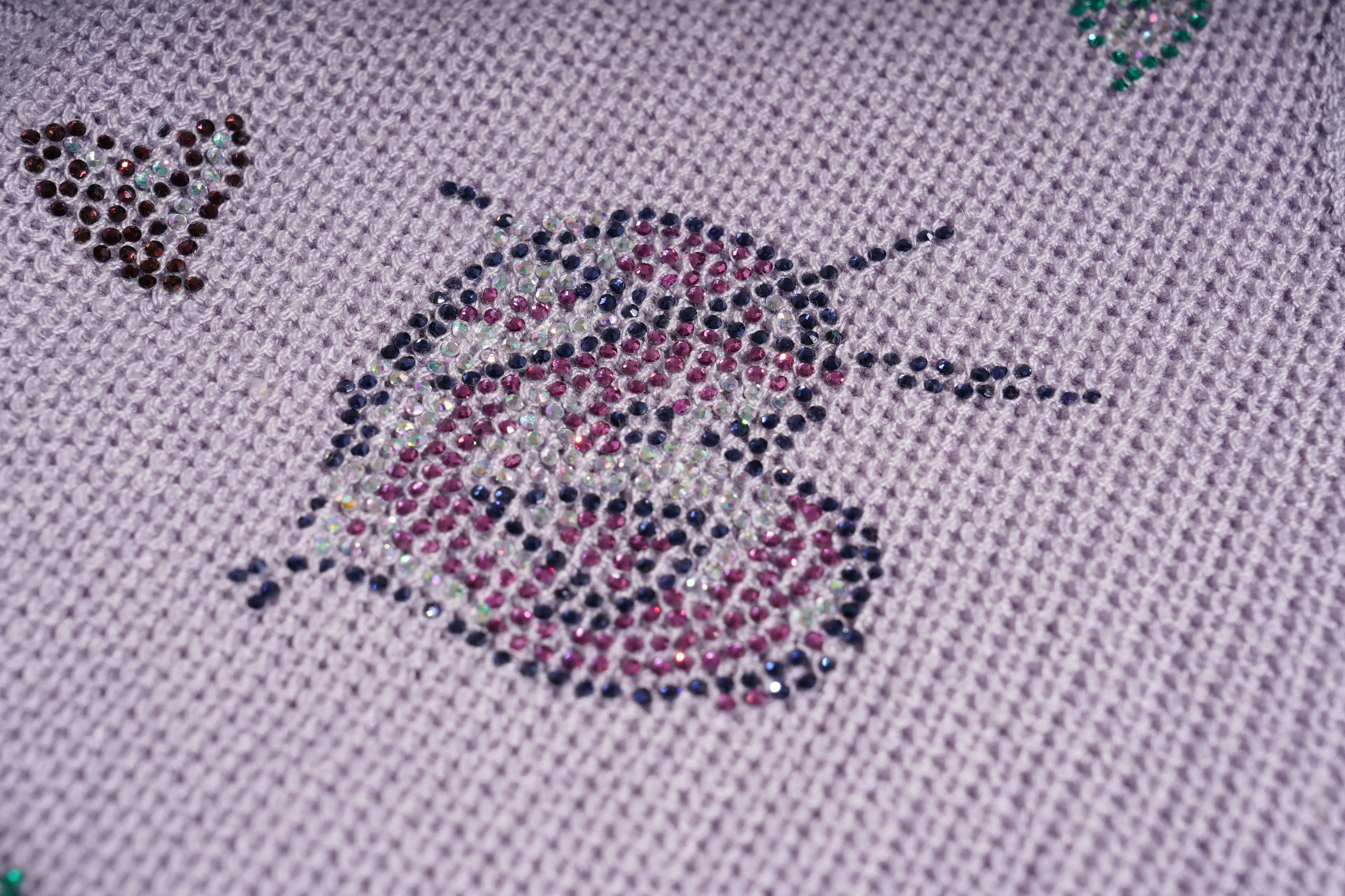 Close-up of a diamond painting canvas with a ladybug design made of small multicolored rhinestones on a light lavender fabric background. TCH Rhinestone Butterfly Knit Twist Top