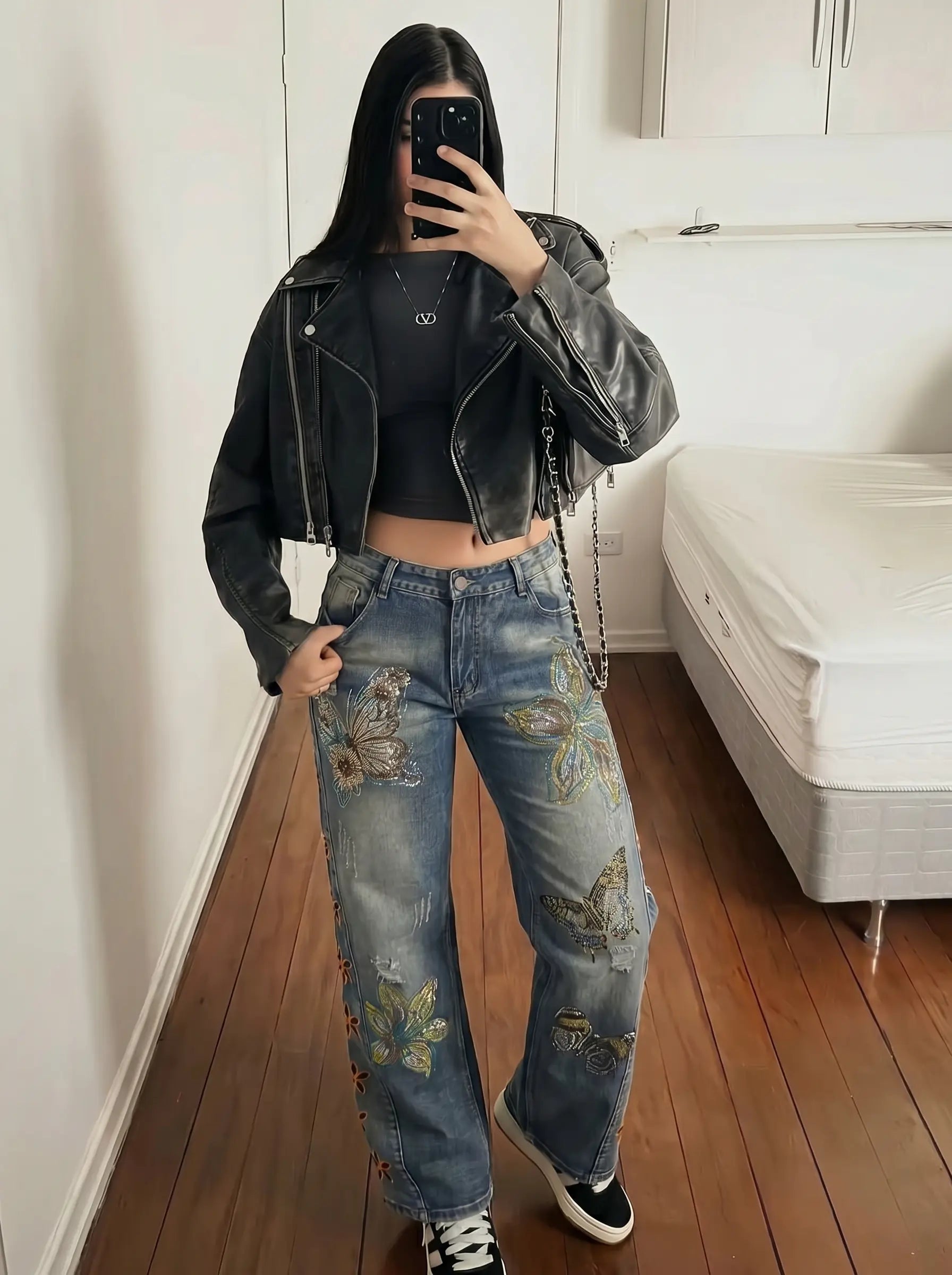 Person wearing a black leather jacket and floral jeans in a bedroom. TCH Rhinestone Butterfly & Lily Distressed Denim Jeans