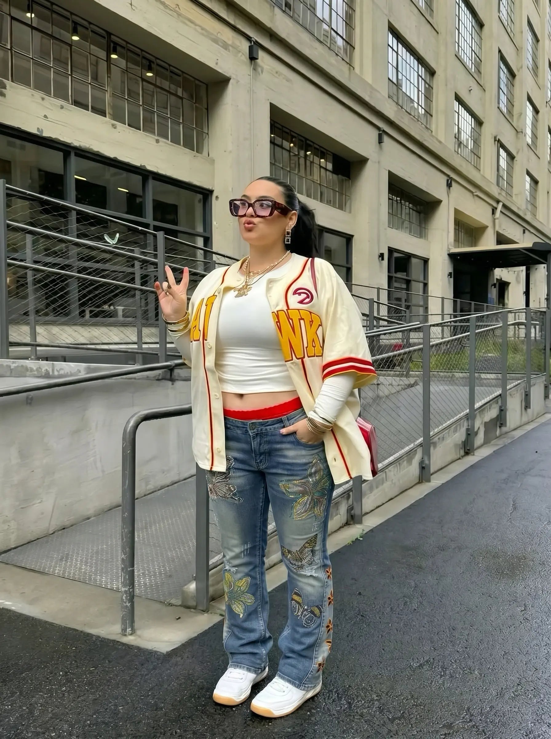 Person wearing a white crop top with red accents and a beige jacket, standing on a street. TCH Rhinestone Butterfly & Lily Distressed Denim Jeans