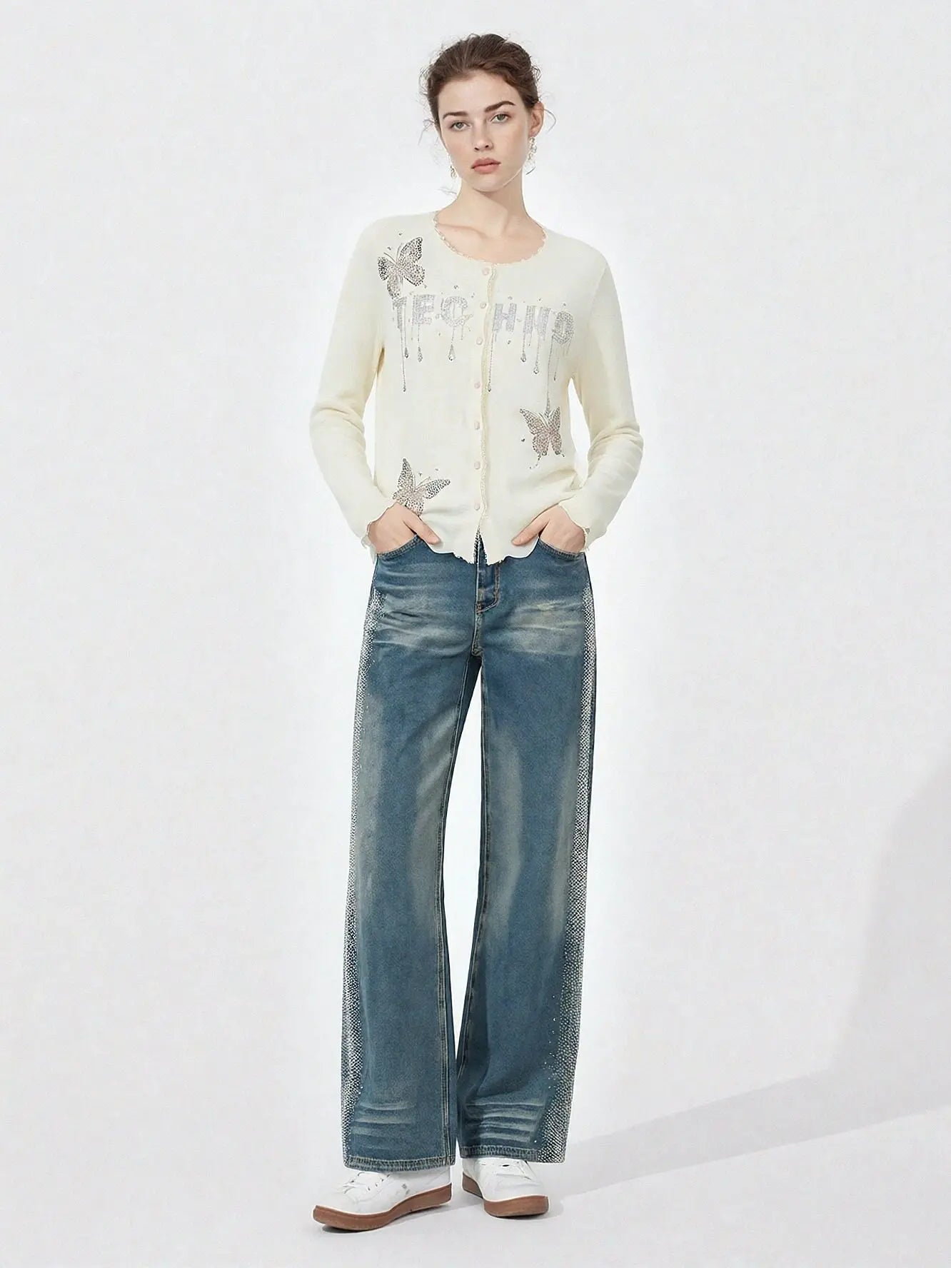 Woman wearing a cream cardigan with text and blue jeans on a white background, TCH Rhinestone Butterfly Logo Knit Cardigan