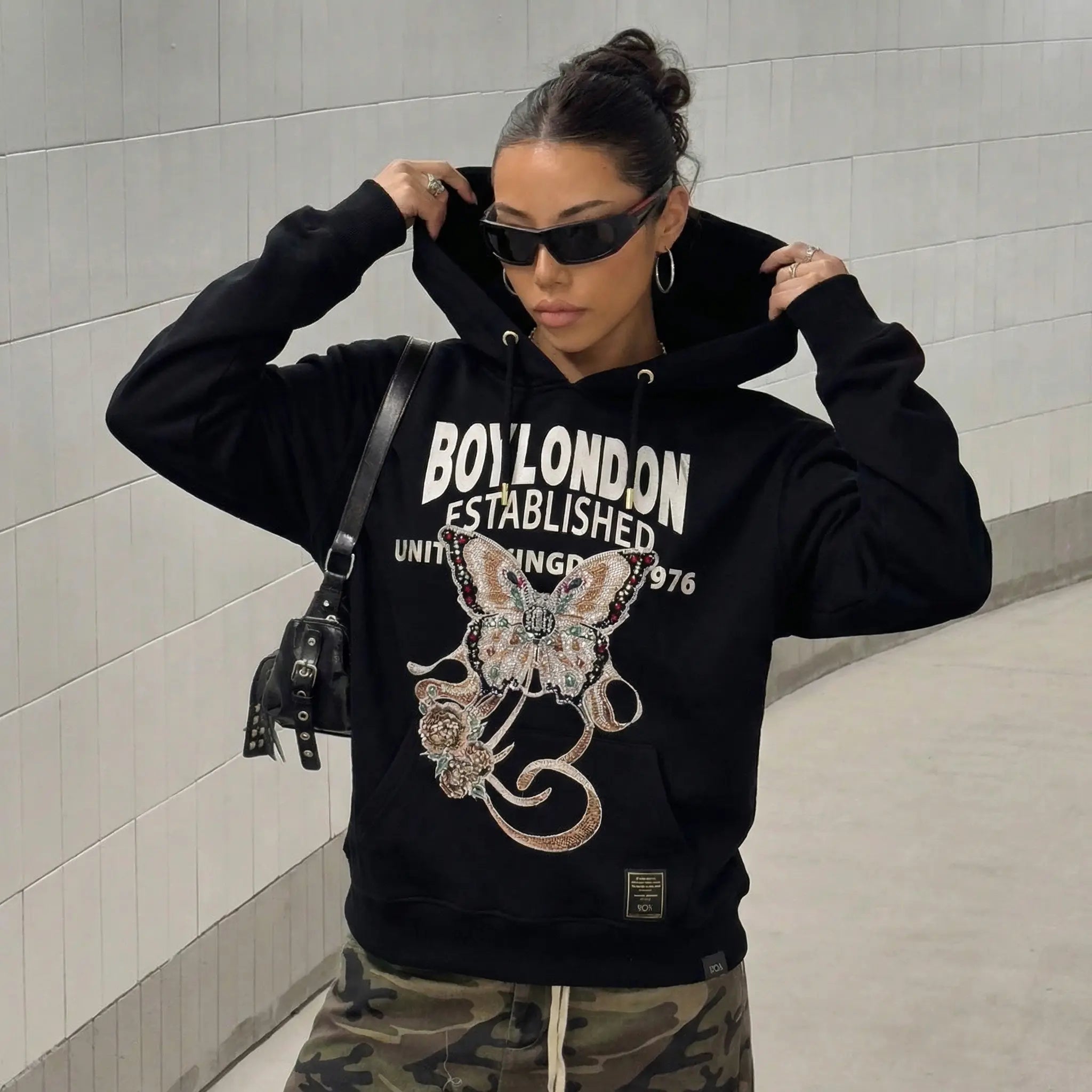 Person wearing a black hoodie with 'Boylondon' text and butterfly design, standing against a tiled wall. TCH Rhinestone Butterfly & Peony Embroidered Hoodie