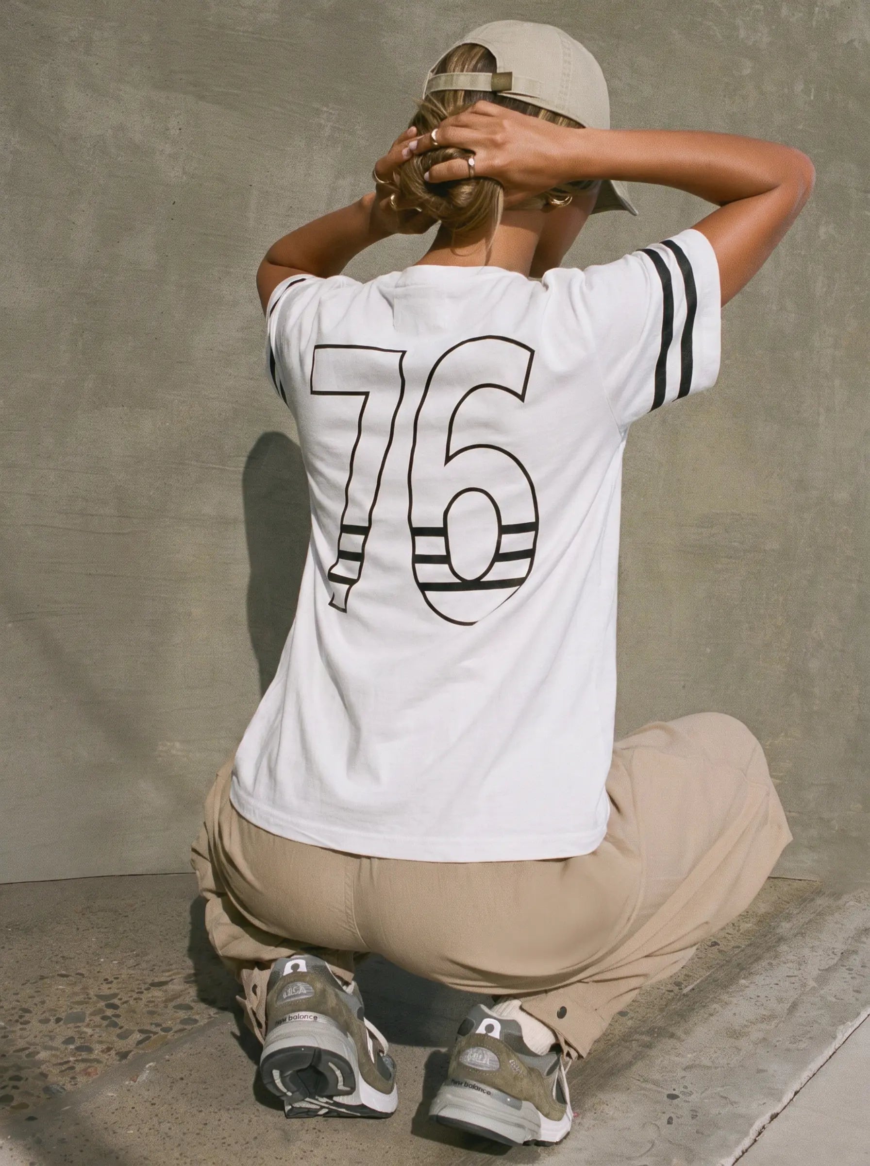 A person crouching against a concrete wall wearing a white short-sleeve T-shirt with a large black outlined '76' on the back, beige pants, and sneakers. TCH Rhinestone Cartoon Pig Graphic Baseball T-Shirt